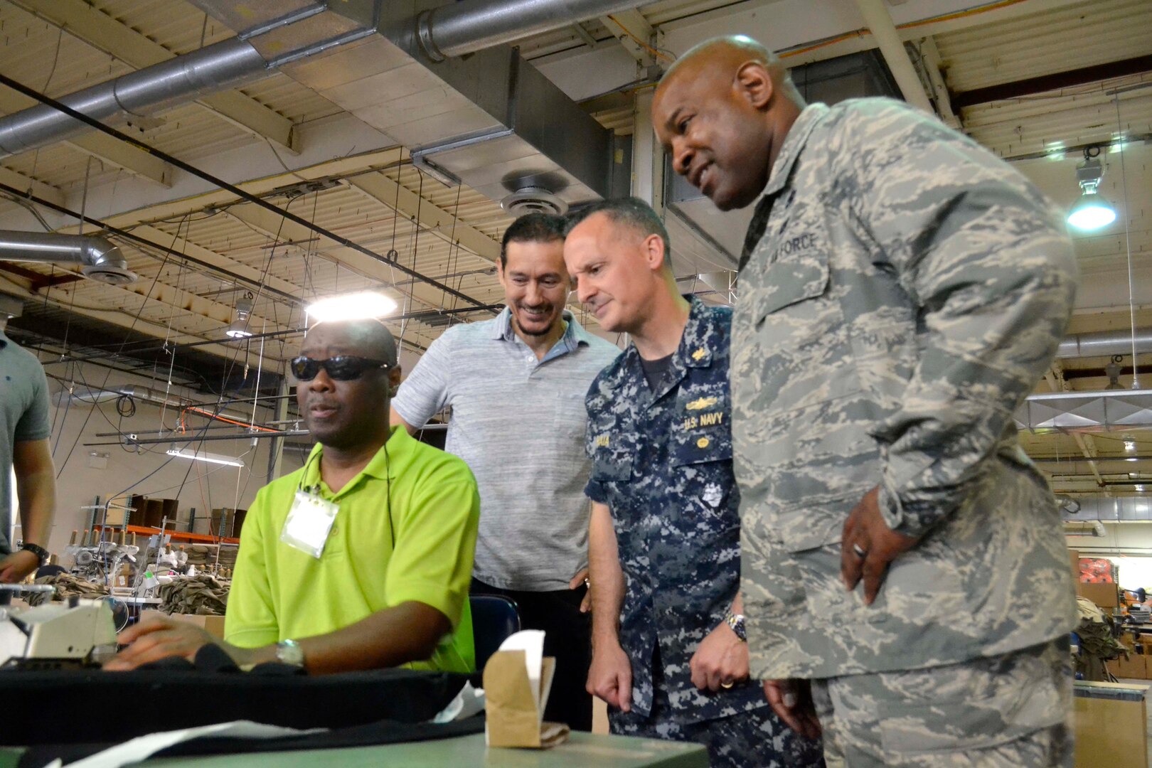 DLA Troop Support C&T Director Air Force Col. Lawrence Hicks, right, and Procurement Process Support Director Navy Capt. Gerald Raia, second right, watch Bestwork Industries for the Blind worker James Woodson, left, sew a Navy fleece jacket with Bestwork production supervisor Carlos Benjumea, in Cherry Hill, New Jersey Sept. 28. Raia, Hicks and C&T Supplier Operations Director Steve Merch, who also attended the visit, were impressed with the synergy of employees on the production line. 