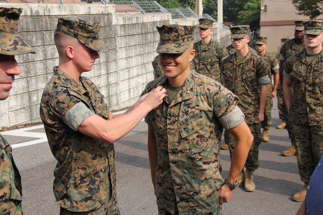 Major Cedric Lee, U. S. Marine Corps Forces Korea AC/S G-6, receives his new rank of Lieutentant Colonle during a promotion ceremony in front of the MARFORK Headquarters building.  Lieutenant Colonel Lee selected the youngest Marine in the G-6 to participate in his pinning to represent the mutual respect and teamwork between enlisted and officer ranks.