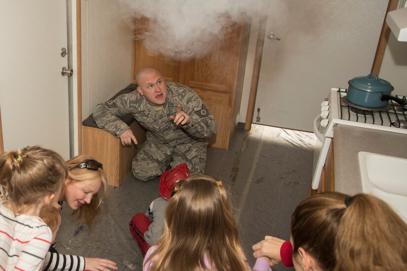 Tech. Sgt. Joseph Mrus, 11th Civil Engineer Squadron fire protection craftsman, points out imitation smoke in a fire safety trailer during a Fire Safety Week demonstration at Joint Base Andrews, Md., Oct. 12, 2016. The trailer set up the scenario of a fire starting in a home and gave participants the chance to call 911, view smoke detectors and escape the building. (U.S. Air Force Photo by Senior Airman Jordyn Fetter)