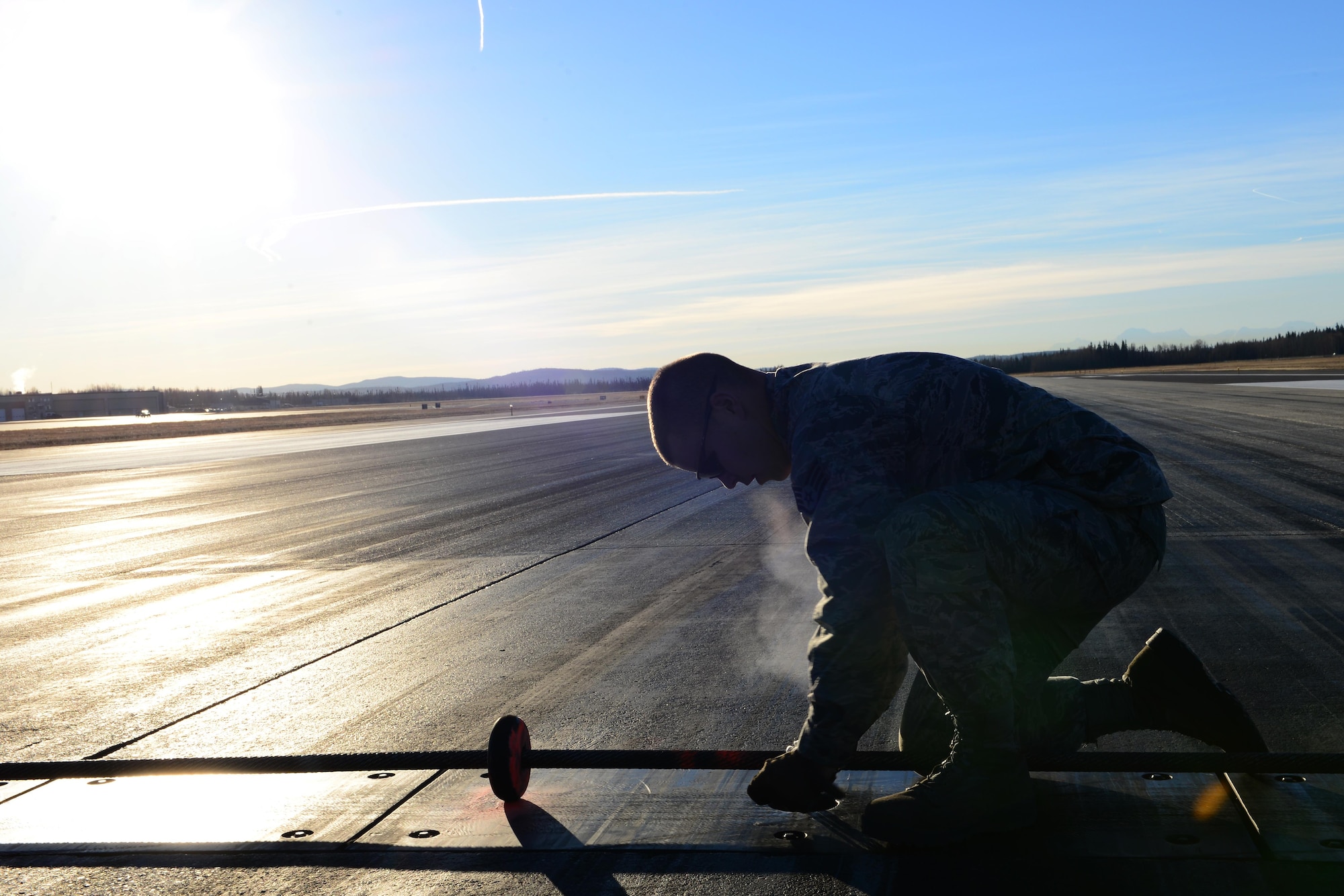 U.S. Air Force Staff Sgt. Jordan Grende, a 354th Civil Engineer Squadron power production journeyman, secures a barrier Oct. 12, 2016, at Eielson Air Force Base, Alaska. Grende tied down the barrier to ensure safe landing of aircraft in case of an in-flight emergency. (U.S. Air Force photo by Airman 1st Class Cassandra Whitman)
