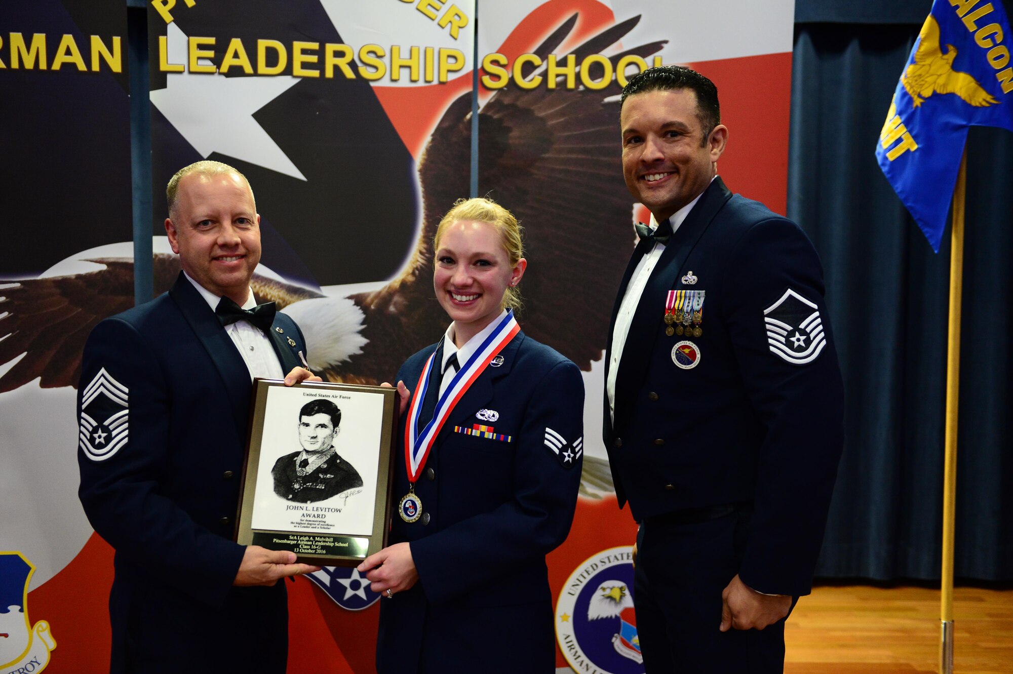 Senior Airman Leigh Mulvihill, 52nd Maintenance Squadron munitions controller, center, receives the John L. Levitow during the Pitsenbarger Airman Leadership School 16-G graduation at Club Eifel on Spangdahlem Air Base, Germany, Oct. 13, 2016. The Levitow award is the highest honor given to the student who displays excellence in all categories of ALS. (U.S. Air Force photo by Senior Airman Joshua R. M. Dewberry)