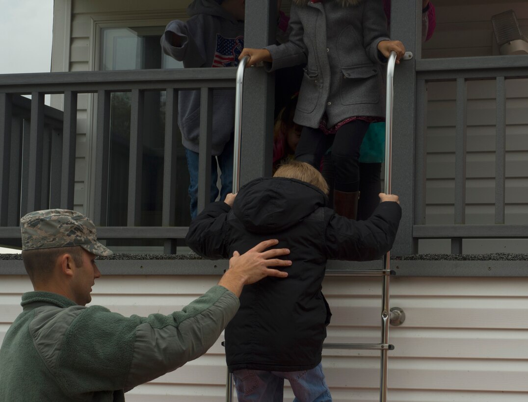 An Airman assigned to the 52nd Civil Engineer Squadron fire department, assists Spangdahlem Elementary School students down a ladder while they practice exiting a building during a fire drill at SES on Spangdahlem Air Base, Germany, Oct. 12, 2016. The pretend house fire taught students what to do if they suspect the house they are in is on fire. (U.S. Air Force photo by Senior Airman Dawn M. Weber)