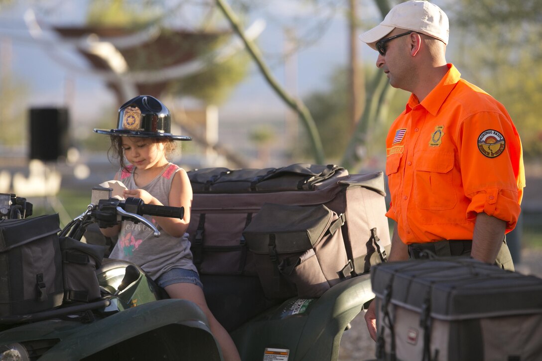 Alexis Weldon, 4, daughter of Special Agent Dennis Weldon, Naval Criminal Investigative Service, sits on off-highway vehicle static display supervised by Albert Hernandez, volunteer, San Bernardino Search and Rescue, during the Night Out Against Crime at Heritage Park aboard Marine Corps Air Ground Combat Center, Twentynine Palms, Calif., Oct. 4, 2016. (Official Marine Corps photo by Cpl. Thomas Mudd/Released)