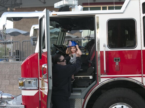 Samantha Vagelatos, firefighter paramedic, Combat Center Fire Department, assists Evern Polizzi, 3, daughter of Staff Sgt. Matthew Polizzi, platoon sergeant, 3rd Battalion, 4th Marines, 7th Marine Regiment, dismount a fire engine during the Night Out Against Crime at Heritage Park aboard Marine Corps Air Ground Combat Center, Twentynine Palms, Calif., Oct. 5, 2016. (Official Marine Corps photo by Cpl. Thomas Mudd/Released)