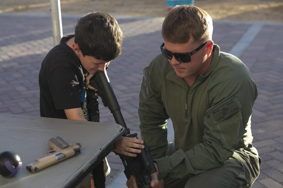 Jeremy Weldon, 7, son of Special Agent Dennis Weldon, Naval Criminal Investigative Service, peers through a rifle optic with Cpl. Jamison Boyer, team member, Special Reaction Team, Provost Marshal’s Office, during the Night Out Against Crime at Heritage Park aboard Marine Corps Air Ground Combat Center, Twentynine Palms, Calif., Oct. 4, 2016. (Official Marine Corps photo by Cpl. Thomas Mudd/Released)