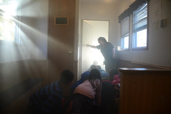 Tiana Bykowski, 775th Civil Engineer Squadron fire inspector, holds a door open for students moving along the floor of a smoke-filled room during Fire Prevention Week at Hill Field Elementary School, Oct. 12. Children learned about kitchen safety, fireplace safety, and escape routes while making their way through the Utah State Fire Marshall's ‘Life Safety House.’ (U.S. Air Force photo by R. Nial Bradshaw)