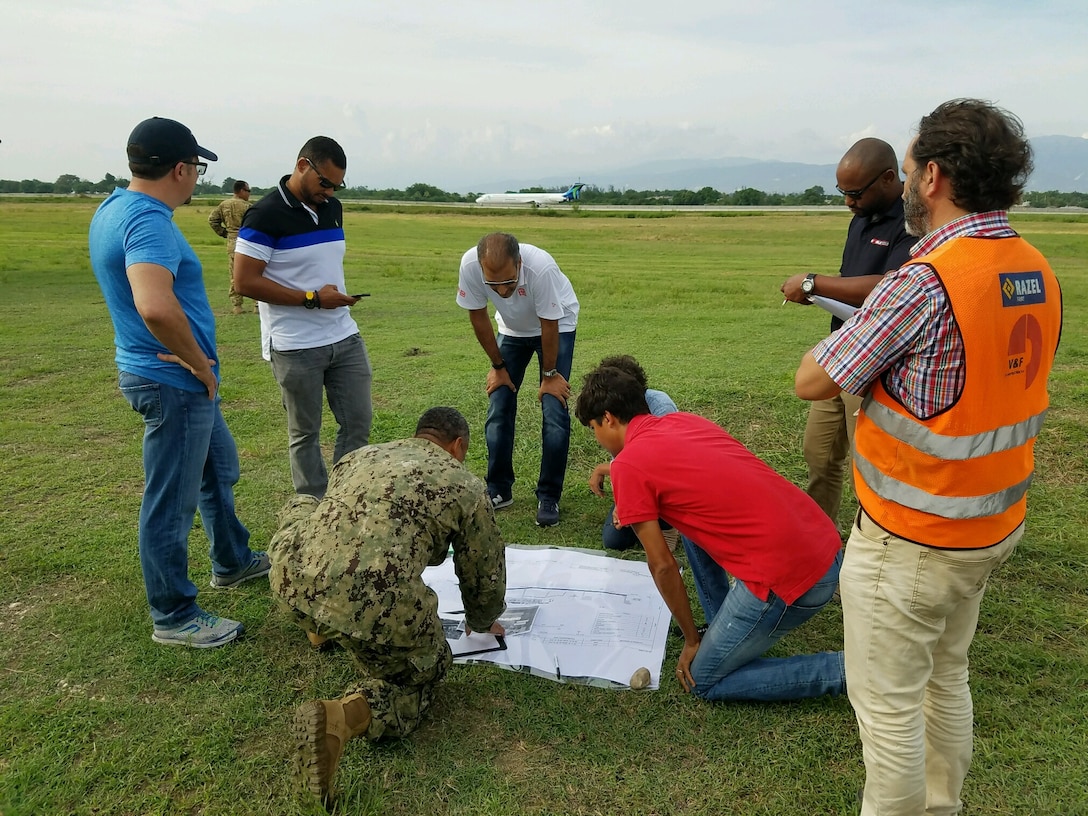 An engineer from the U.S. Naval Construction Forces "Seebees" (center, in fatigues) and personnel from a DLA Troop Support contractor review plans for a helicopter pad at Toussaint L'Ouverture International Airport, Port au Prince, Haiti, October 2016.