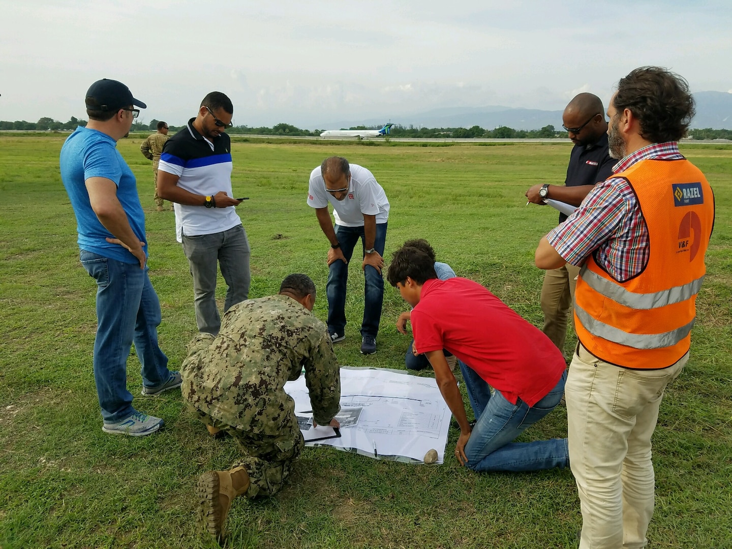 An engineer from the U.S. Naval Construction Forces "Seebees" (center, in fatigues) and personnel from a DLA Troop Support contractor review plans for a helicopter pad at Toussaint L'Ouverture International Airport, Port au Prince, Haiti, October 2016.