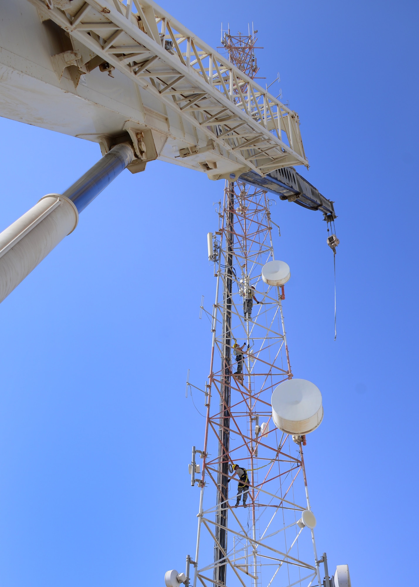 Airmen from the 379th Expeditionary Communications Squadron and 379th Expeditionary Civil Engineer Squadron climb up a radio tower Oct. 8, 2016, at Al Udeid Air Base, Qatar. The Airmen were working to remove several inactive microwave dish transmitters from the tower due to structural integrity concerns. The transmitters weighed up to 200 pounds each and required the use of a Terex RT 780 crane in order to safely bring them down to the ground once detached. (U.S. Air Force photo/Senior Airman Miles Wilson/Released)