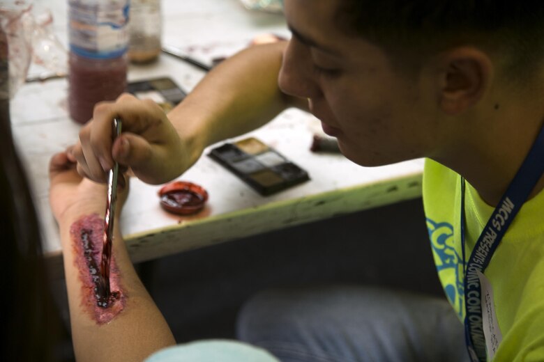 Cpl. Jose Torrijos paints zombification makeup on an attendee October 15 during Comic Con on Camp Foster, Okinawa, Japan. Comic Con is an annual event that takes place for comic book connoisseurs, video gamers, movie fans and artists across the island to unite and bond with each other in their passions and interests. Torrijos, an Oakland, California native is a volunteer makeup artist for Comic Con, and supply admin clerk with Marine Corps Installations Pacific-Marine Corps Base Camp Butler, Japan. (U.S. Marine Corps photo by Cpl. Brittany A. James / Released) 