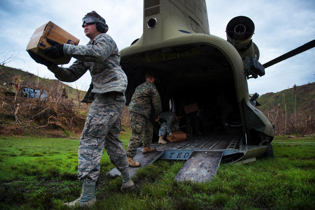 Air Force Airman First Class James Raynor, left, tosses a box during a relief mission in Anse d'Hainault, Haiti, Oct. 14, 2016. Raynor is an air transportation apprentice assigned to the 621st Contingency Response Wing. Air Force photo by Staff Sgt. Paul Labbe