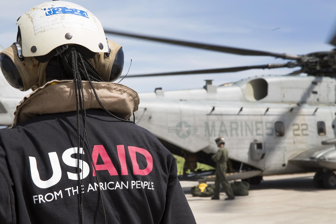 A member of the United States Agency for International Development’s Disaster Assistance Response Team watches U.S. service members load relief supplies onto a CH-53E Super Stallion helicopter at Port-au-Prince, Haiti, Oct 16, 2016. The Marines and sailors assigned to the 24th Marine Expeditionary Unit aboard the USS Iwo Jima have been providing assistance to the U.S. government’s civil humanitarian aid and disaster relief efforts in Haiti in the wake of Hurricane Matthew. Marine Corps photo by Cpl. Hernan Vidana