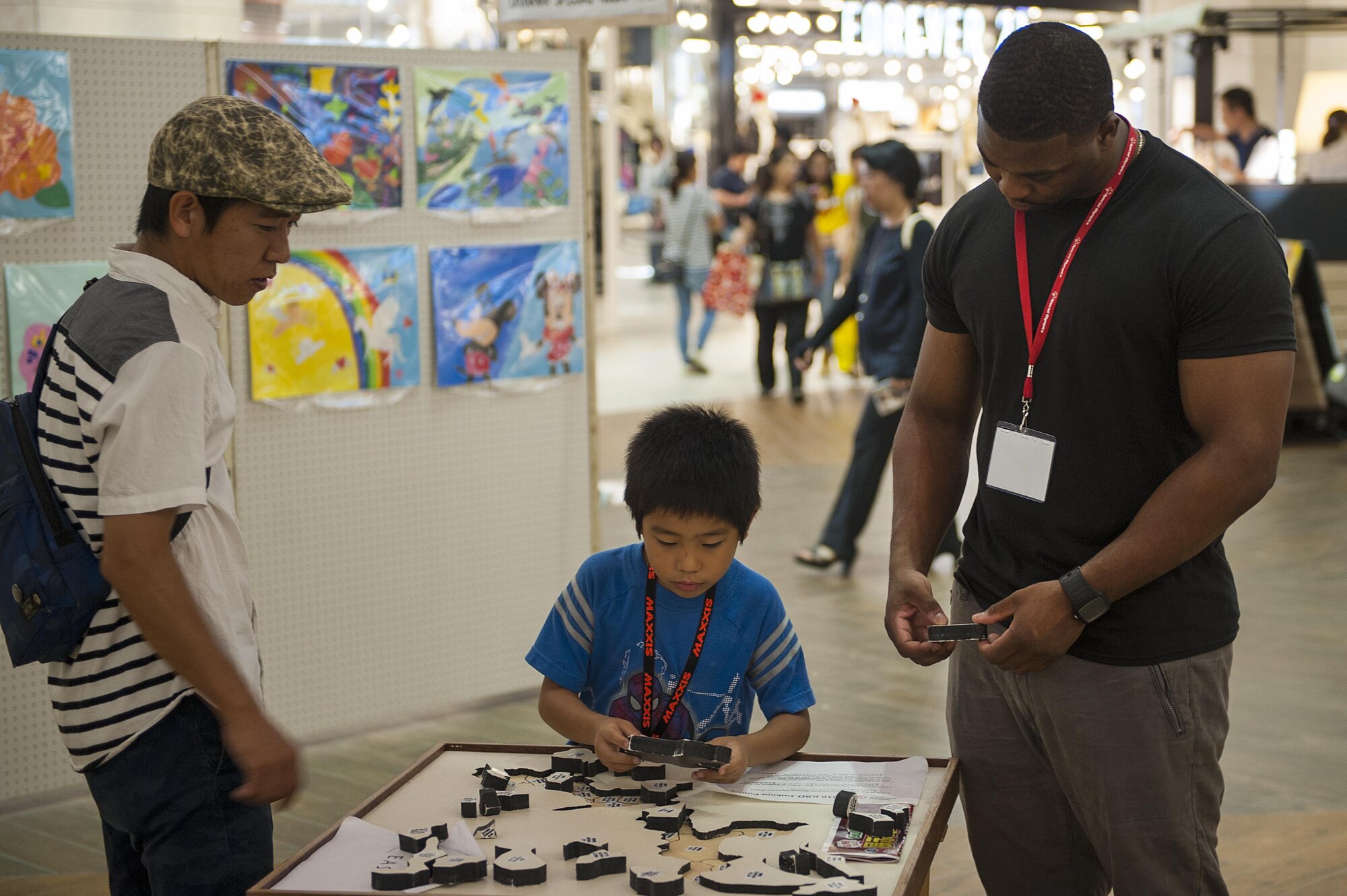 U.S. Air Force Staff Sgt. Elmore Norwood, 18th Equipment Maintenance Squadron aircraft structural maintainer, helps an Okinawan child complete a puzzle during the Kadena Special Olympics Art Exhibition at the Rycom Mall Oct. 16, 2016 in Okinawa, Japan. This is the 10th annual KSO Art Exhibition where event organizers display art made by Okinawan children with special needs is put on display. (U.S. Air Force photo by Airman 1st Class Corey M. Pettis)
