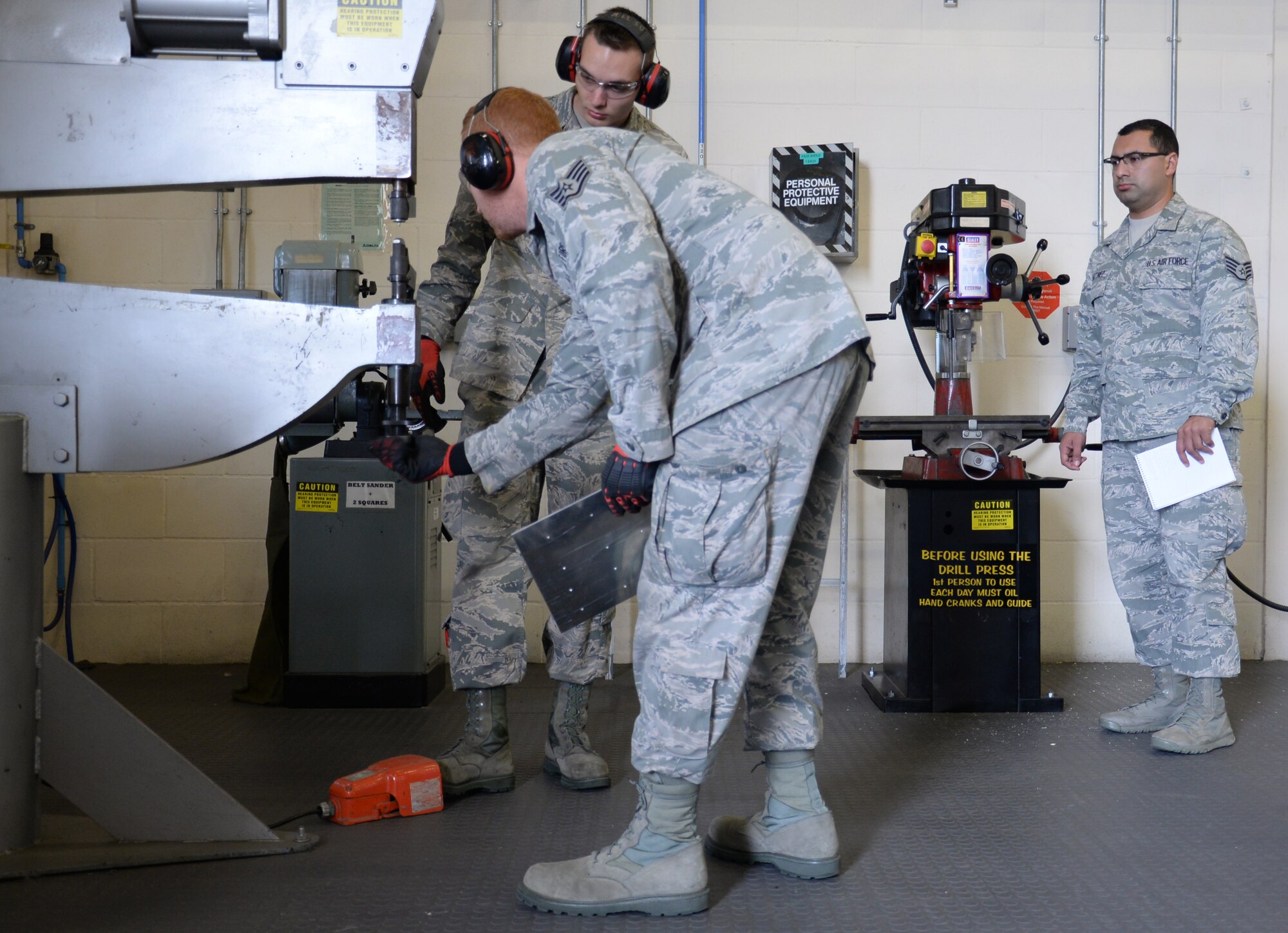 U.S. Air Force Staff Sgt. Jose Martinez, right, 100th Air Refueling Wing NCO in charge of inspections and analysis, observes U.S. Air Force Staff Sgt. Zachary Sidlovsky, front, 100th Maintenance Squadron Aircraft Structural Maintenance craftsman, and U.S. Air Force Airman 1st Class Devon Postlewait, 100th MXS ASM apprentice, while they modify a piece of sheet metal Oct. 17, 2016, on RAF Mildenhall, England. Before operating the machinery the Airmen put on the correct personal protective equipment. (U.S. Air Force photo by Gina Randall)