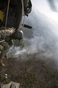 Alaska Army National Guard Spc. Tanner Lauderback, a crew chief with 1st Battalion, 207th Aviation Regiment, keeps a line of sight on the bucket attached to a UH-60 Black Hawk helicopter as he prepares to release water during a firefighting mission near Cooper Landing, Alaska, June 17, 2015. Some Alaska Air Guard members are fighting the Moose Creek Fire this week.