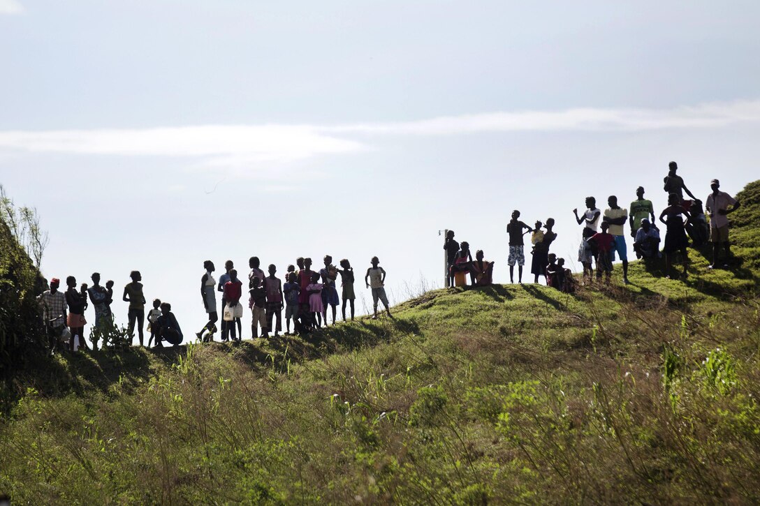 Haitian residents watch from a hillside as U.S. troops unload humanitarian supplies from an MH-60 Seahawk helicopter at LaCohaune, Haiti, Oct. 17, 2016. Marine Corps photo by Sgt. Justin T. Updegraff
