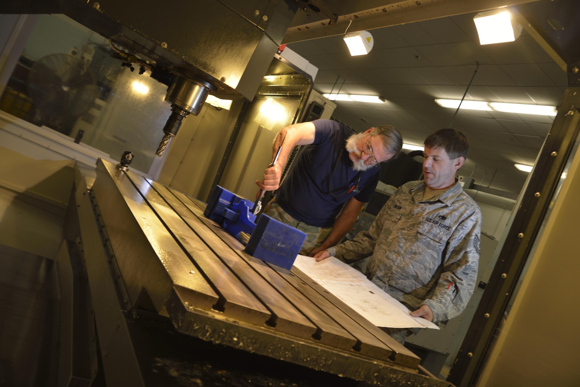 Mr. Gary Surozenski and Tech Sgt. Richard Towlson stand at the opening of the milling machine doing intricate measurements of the wax first-run copy of the C-5 elevator support bracket.