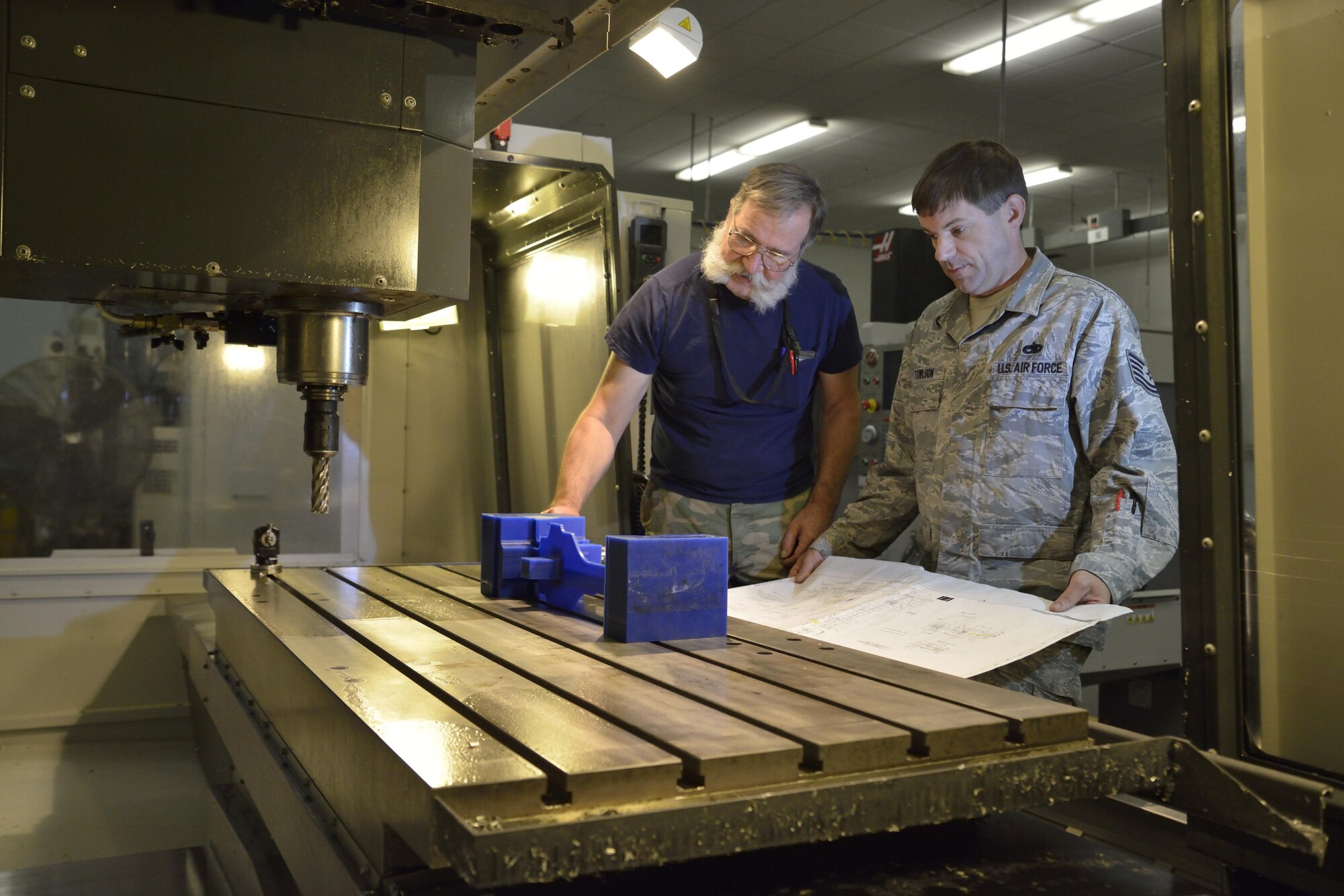 Mr. Gary Surozenski and Tech Sgt. Richard Towlson stand at the opening of the milling machine doing intricate measurements of the wax first-run copy of the C-5 elevator support bracket.
