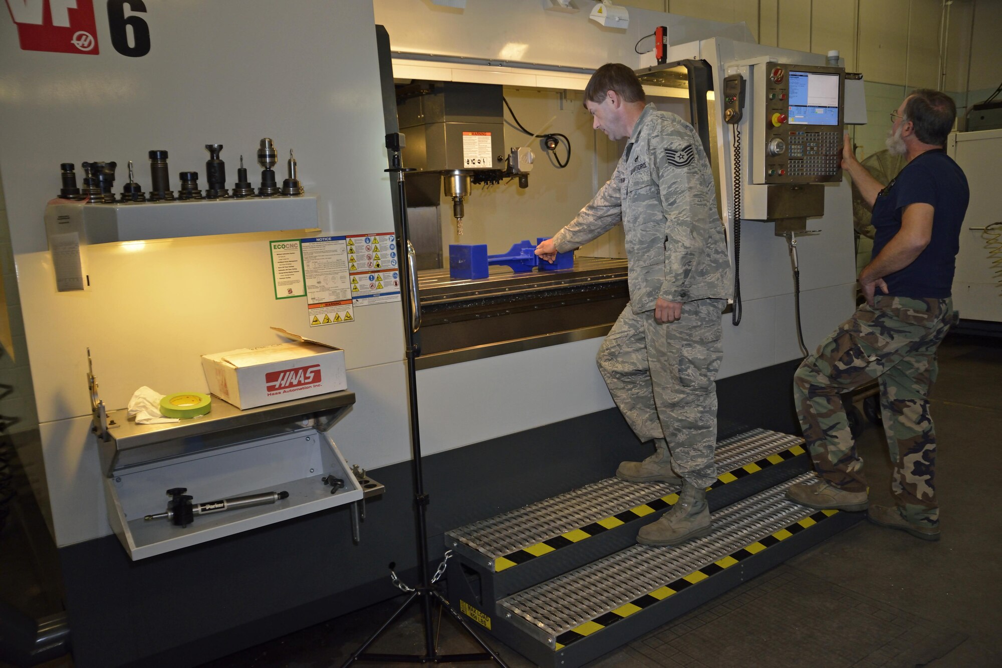 Mr. Gary Surozenski and Tech Sgt. Richard Towlson stand at the opening of the milling machine doing intricate measurements of the wax first-run copy of the C-5 elevator support bracket.