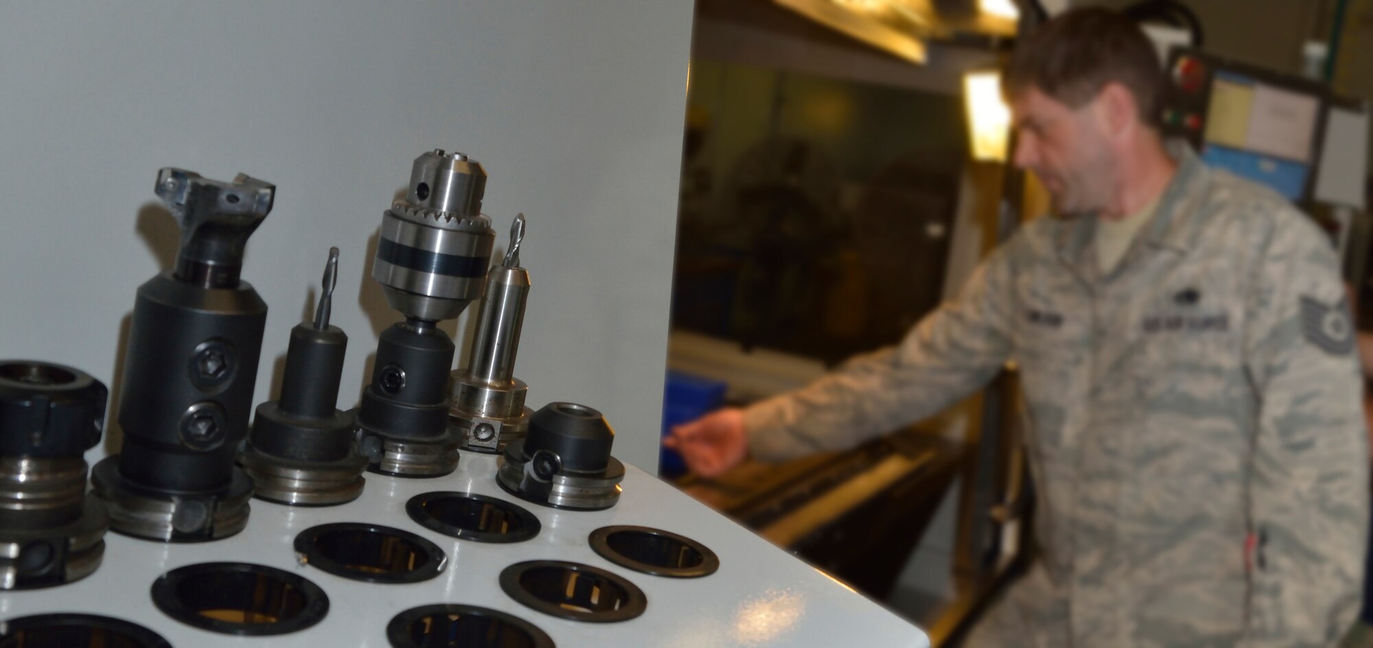 Tech Sgt. Richard Towlson stands at the opening of the milling machine doing intricate measurements of the wax first-run copy of the C-5 elevator support bracket.