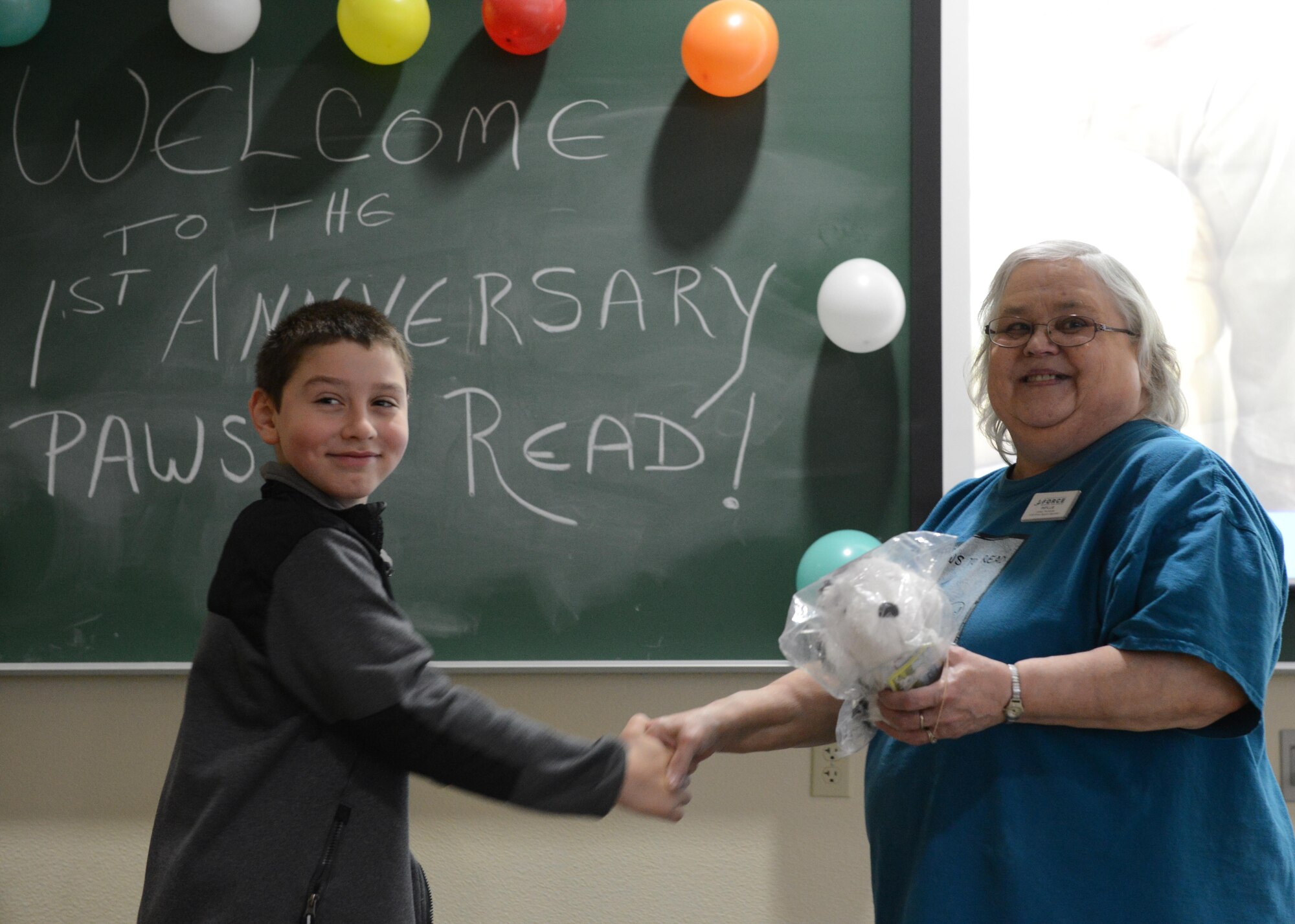 Phyllis Talas, 673d Force Support Squadron library technician, presents an award to Aiden Patterson, 8, at the Paws to Read one-year celebration at the Joint Base Elmendorf-Richardson library, Oct. 15, 2016. Aiden has attended all Paws to Read sessions and received the award for his commitment to the program. 