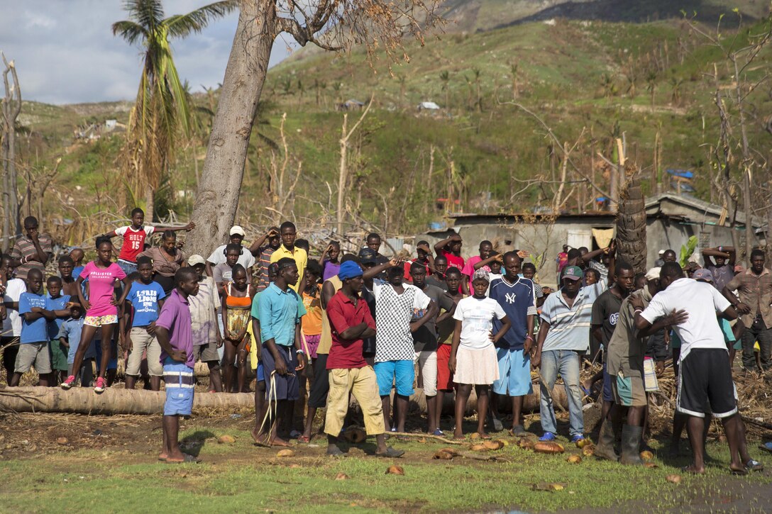 Haitian residents gather near the landing zone and watch as U.S. troops and volunteers unload humanitarian supplies from an MH-60 Seahawk helicopter at LaCohaune, Haiti, Oct. 17, 2016. Marine Corps photo by Sgt. Justin T. Updegraff
