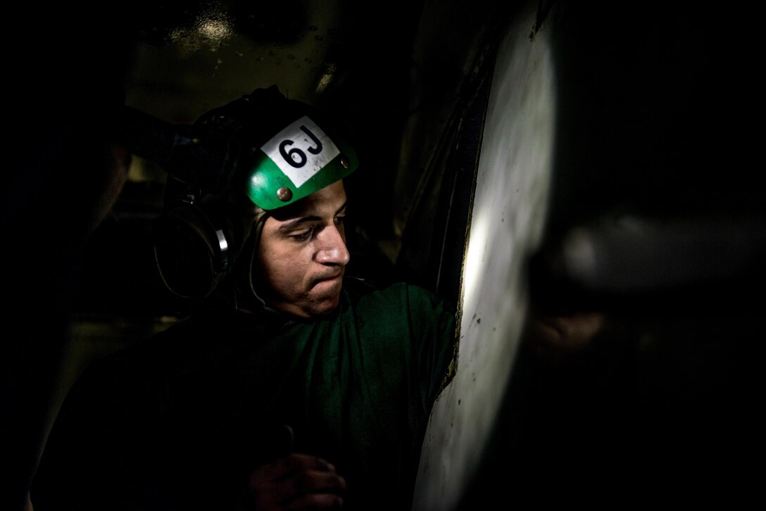 Navy Petty Officer 2nd Class Marco Cheaib reaches into an access panel of the "hot section" of an E2-C Hawkeye's engine in the hangar bay of the USS Ronald Reagan during Invincible Spirit, an exercise off the southern coast of South Korea, Oct. 13, 2016. The aircraft is assigned to Airborne Early Warning Squadron 115. Navy photo by Petty Officer 3rd Class Nathan Burke 