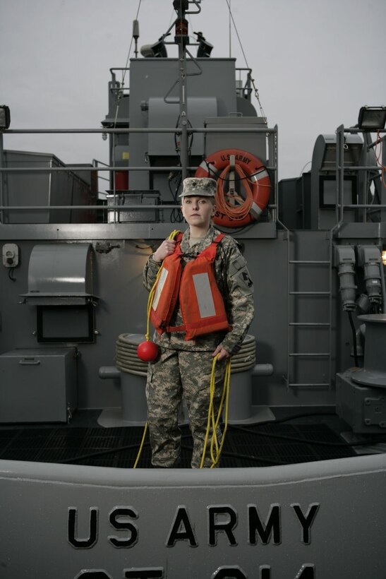 A Soldier wearing ACU and life vest standing on deck on back of tug boat holding rope.