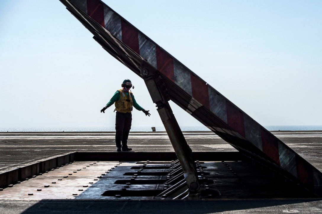 Navy Petty Officer 2nd Class Ricardo Rodriguez signals to lower a jet blast deflector on the flight deck of the aircraft carrier USS Dwight D. Eisenhower in the Persian Gulf, Oct. 16, 2016. Rodriguez is an aviation boatswain's mate (equipment). Navy photo by Petty Officer 3rd Class Robert J. Baldock