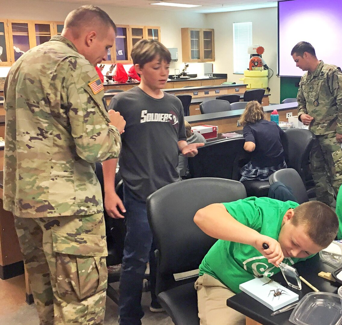 Capt. Travis Gilchriest (left), Preventive Medicine Specialist Program entomology instructor at the Medical Education and Training Campus at Joint Base San Antonio-Fort Sam Houston, talks with a student from the River City Believers Academy while another student uses a magnifying glass to examine a pinned insect Sept. 30.