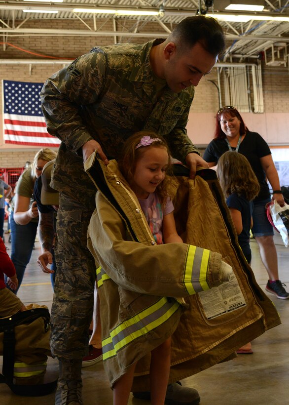 Airman First Class Andrew Garcia, 56th Civil Engineer Squadron firefighter, helps a child put on firefighter gear during the 56th Civil Engineer Squadron fire station open house, Oct. 15, 2016 at Luke Air Force Base, Ariz. The fire station open house was available to the public and featured free food, displays, demonstrations and games for children.(U.S. Air Force photo by Senior Airman Devante Williams)