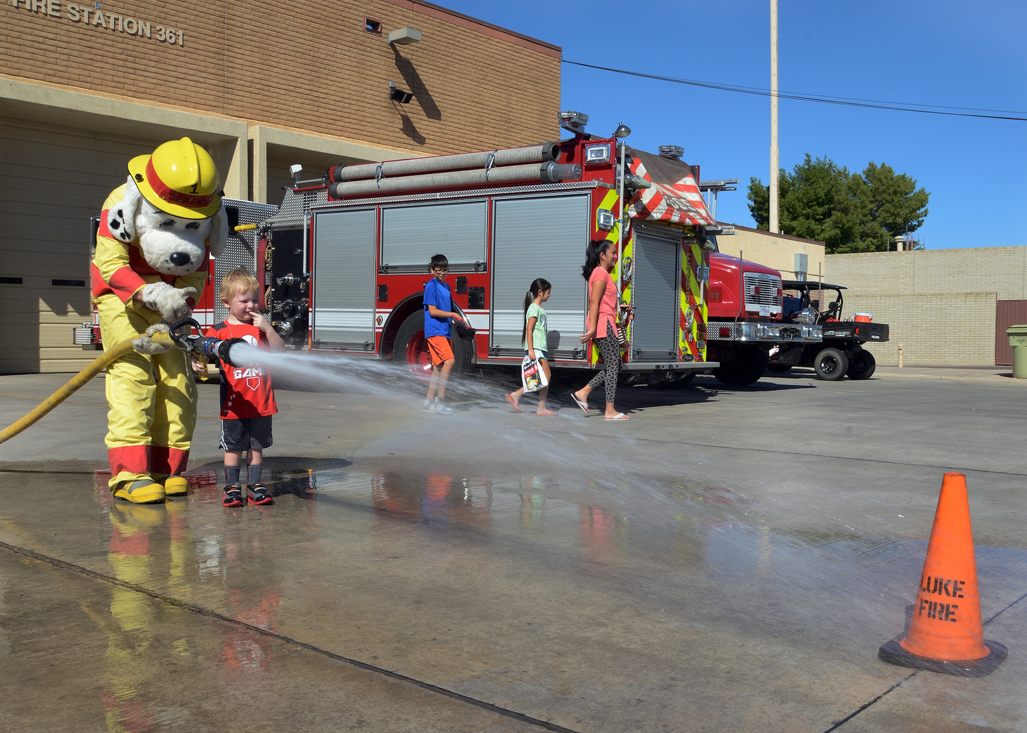 Sparky, the fire dog, helps Donnie McGuire, 3, son of Staff Sgt. Donald McGuire, 944th Civil Engineer Squadron firefighter, knock down an orange cone with a fire hose during the 56th Civil Engineer Squadron fire department open house Oct. 15, 2016 at Luke Air Force Base, Ariz. The fire station open house was available to the public and featured free food, displays, demonstrations and games for children. (U.S. Air Force photo by Senior Airman Devante Williams)
