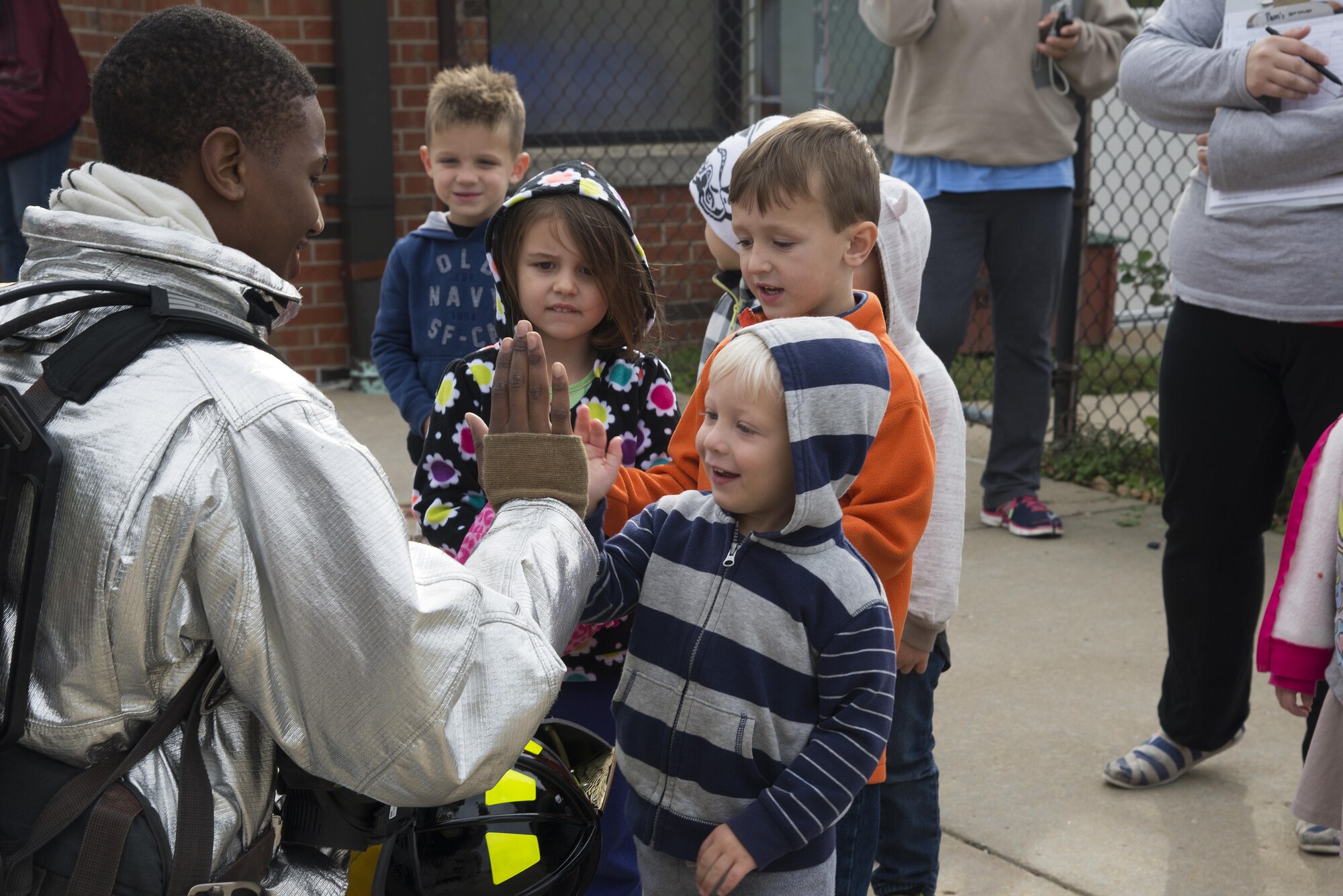 A1C Markland Hunter, 375th Civil Engineering Squadron firefighter, highfives a child after showing the children his fire suit during fire prevention week, October 14, 2016 at the Child Development Center.This year’s Fire Prevention Week campaign, “Don’t Wait – Check the Date! Replace Smoke Alarms Every 10 Years,” represents the final year of our three-year effort to educate the public about basic but essential elements of smoke alarm safety.(U.S. Air Force photo by Airman Gwendalyn Smith)