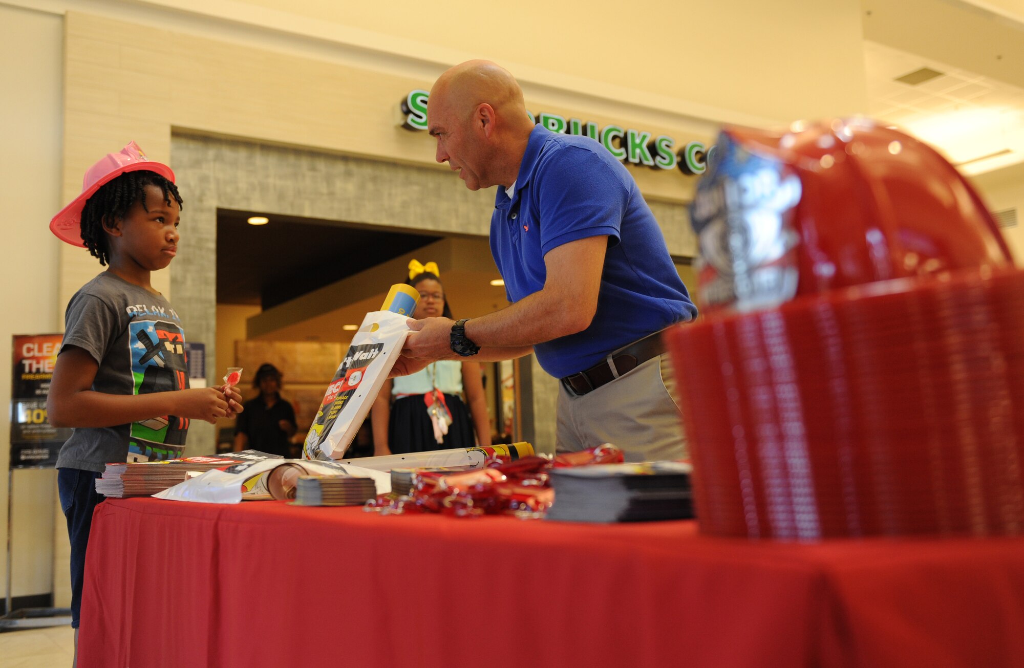Bill McCoy, Army and Air Force Exchange Service lost prevention manager, gives a goody bag to Salayia Edwards, daughter of Staff Sgt. Marlena Gordon, 6th Dental Squadron dental technician, MacDill Air Force Base, Fla., during Fire Prevention Week at the Base Exchange Oct. 11, 2016, on Keesler Air Force Base, Miss. The week-long event included fire drills, literature hand-outs and stove fire demonstrations around the base and concluded with an open house at the fire department. (U.S. Air Force photo by Kemberly Groue/Released)