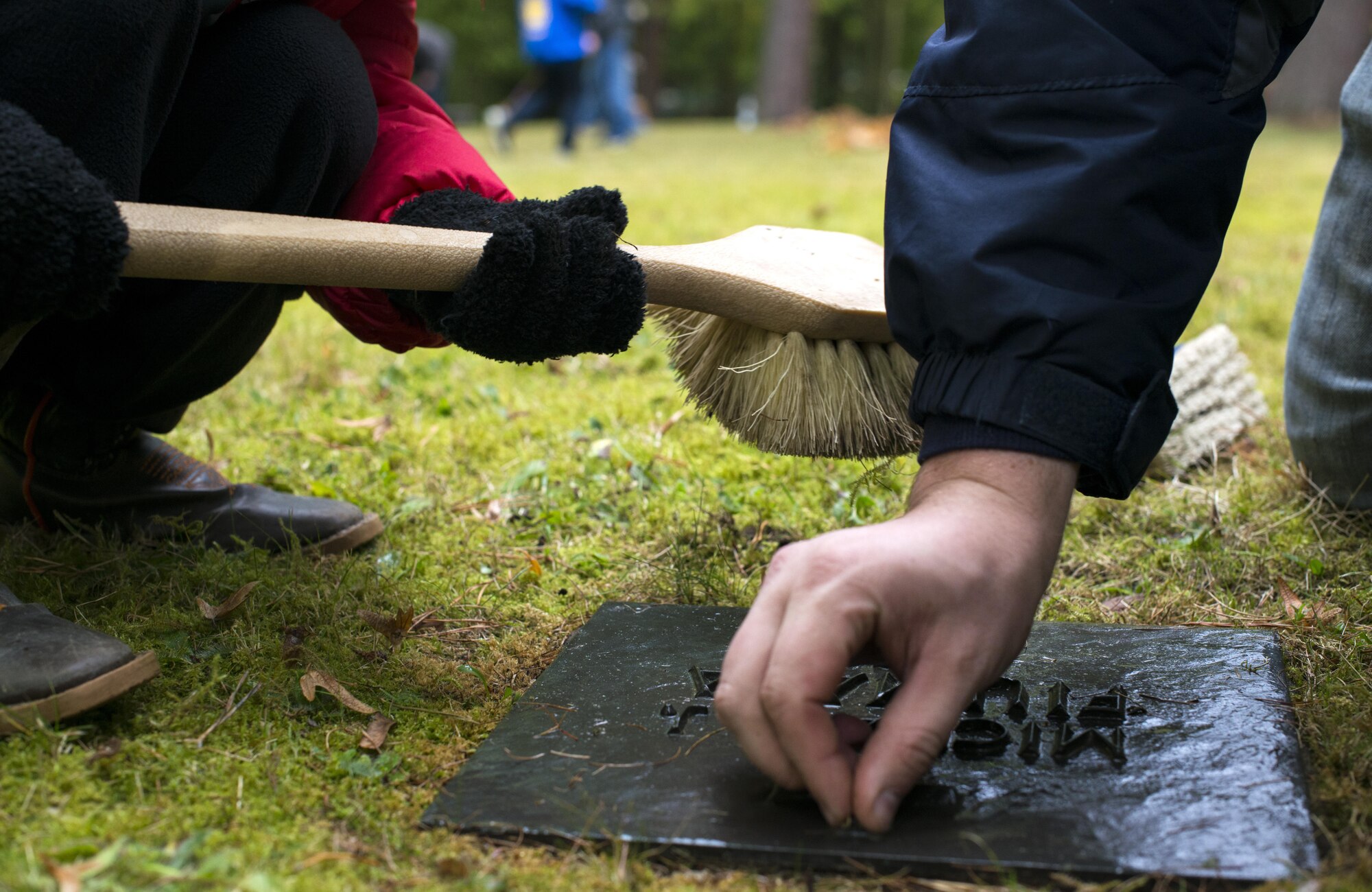 Senior Airman Patrick McGuffin, 86th Operations Support Squadron air traffic controller, and his son, Eli, brush dirt off a gravestone at the American Kindergraves in Kaiserslautern, Germany, Oct. 15, 2016. Volunteers brushed and polished each of the more than 450 gravestones at the site. (U.S. Air Force photo by Senior Airman Tryphena Mayhugh)