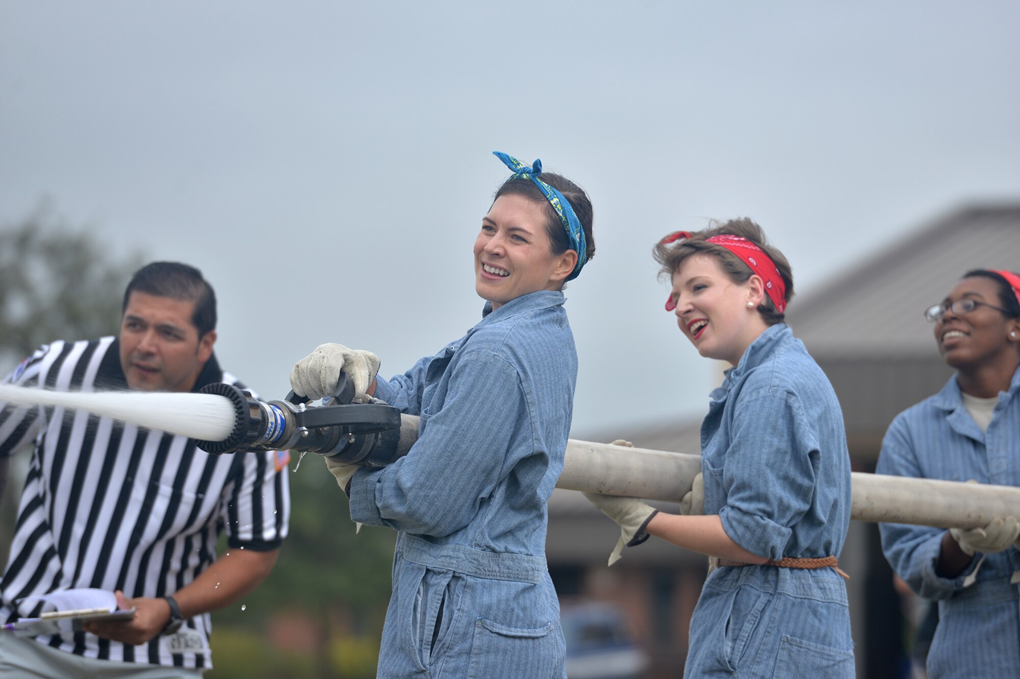 Joe Mendez, 17th Civil Engineer Squadron combat equipment fighting order, watches U.S. Air Force Senior Airman Laurel Richards, 17th Training Wing Public Affairs broadcaster, Airman 1st Class Caelynn Ferguson, 17th TRW/PA photojournalist and 2nd Lt. Tisha Wilkerson, 17th TRW/PA officer, use a fire hose during the Annual Fire Muster Challenge at Goodfellow Air Force Base, Texas, Oct. 14, 2016. Participants had to carry a charged, three-inch fire hose and shoot targets to complete the challenge. (U.S. Air Force photo by Airman 1st Class Randall Moose/Released)
