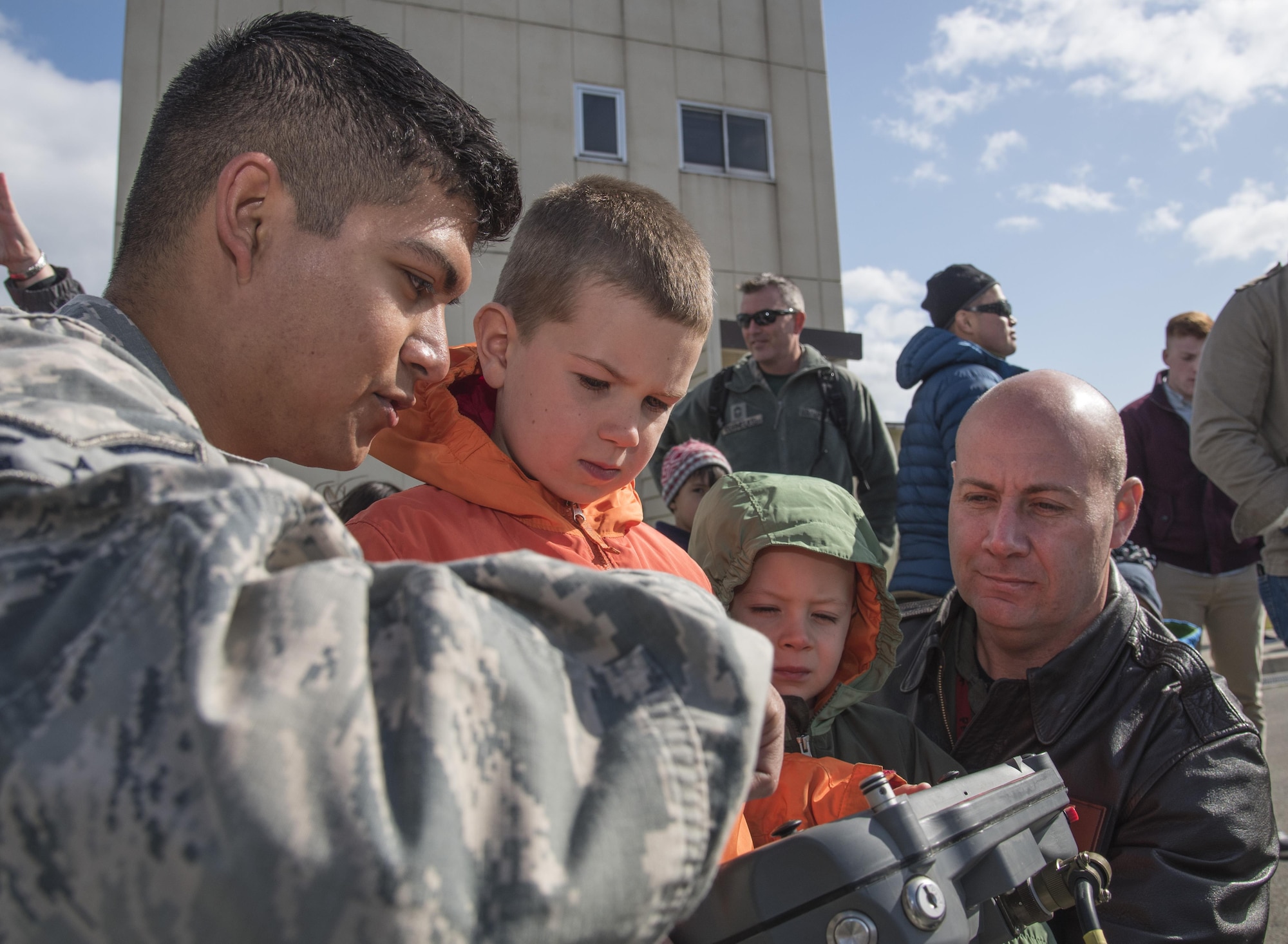 Senior Airman Manuel Carvajo,left, a 35th Civil Engineer Squadron explosive ordnance disposal technician, shows Isaac, center left, and Sam Tolk, center right, both sons of Maj. David Tolk, right, a 13th Fighter Squadron pilot, how to operate a remote control to an EOD reconnaissance devide during a Range Day event at Misawa Air Base, Japan, Oct. 21, 2016. Various shops, including weather, aircrew flight equipment and security forces, displayed tools used to accomplish the mission. (U.S. Air Force photo by Airman 1st Class Sadie Colbert)