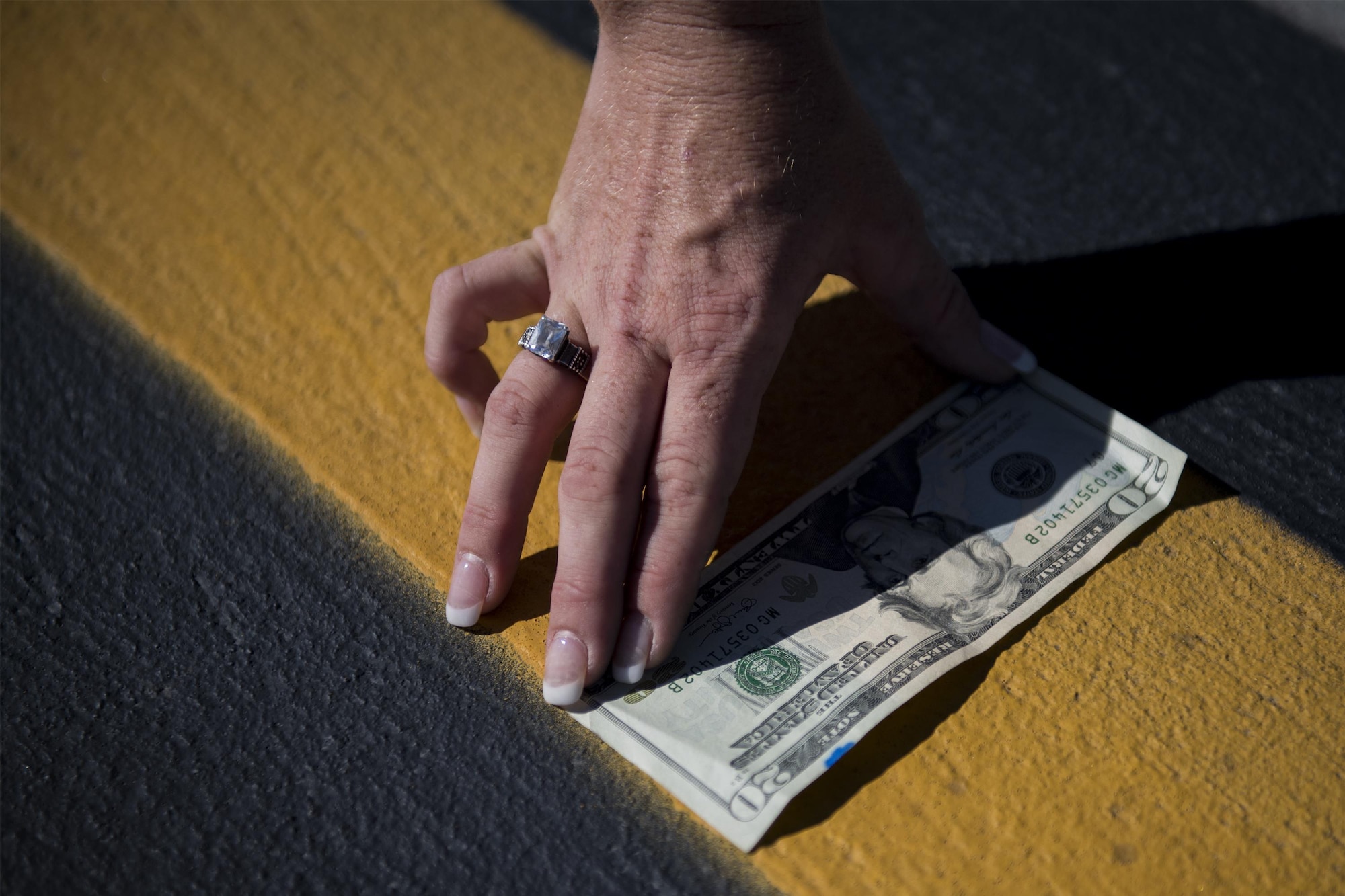 Support Squadron NCO in charge of airfield management operations, demonstrates a way to ensure painted flightline lines fit the regulation width, Oct. 19, 2016, at Moody Air Force Base, Ga. She did this by holding a $20 bill to the line due to the fact that they are both six inches. Precise measurements regulate every line and marking found on the flightline to ensure the safety of Airmen and aircraft. (U.S. Air Force photo by Airman 1st Class Daniel Snider)