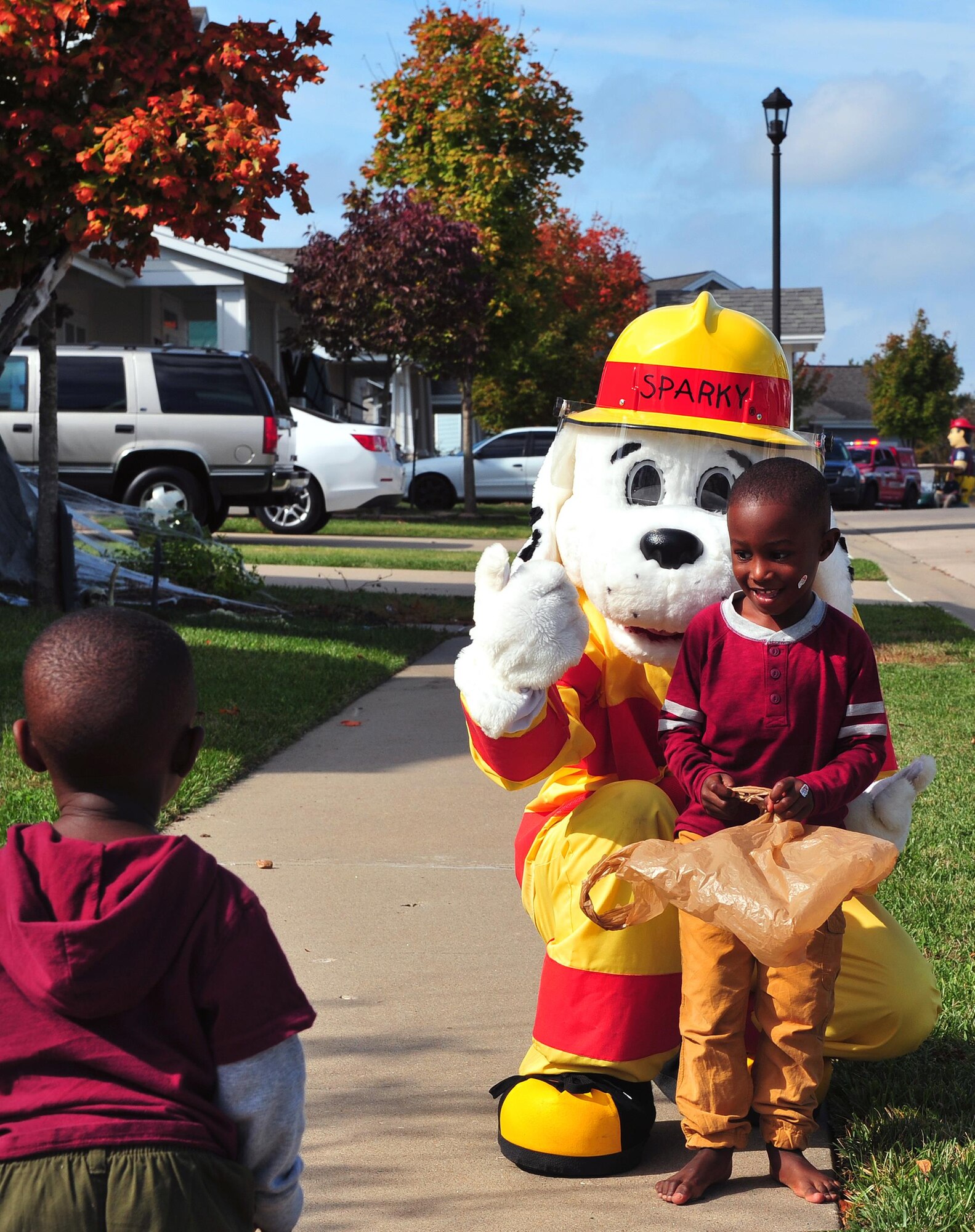 Spark the Dog, a fire prevention mascot, hugs a Whiteman youth and awaits another to join for a group photo at Whiteman Air Force Base, Mo., Oct. 15, 2016. Members of Team Whiteman along with the fire prevention mascots met with families and passed candy to youth as part of the parade finale. (U.S. Air Force photo by Senior Airman Jovan Banks)