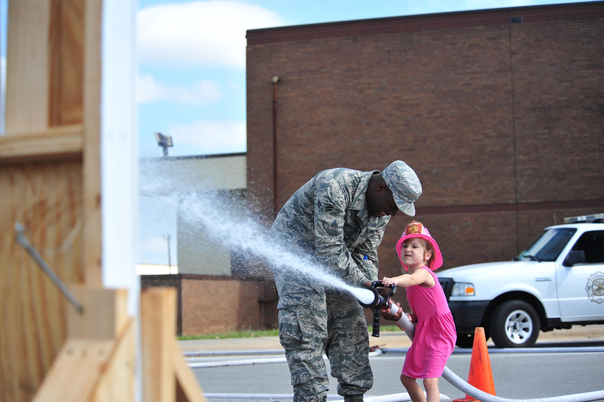 A firefighter assigned to the 509th Civil Engineer Squadron assist a Whiteman youth in using a fireman’s hose to demonstrate firefighting techniques. The fire prevention week finale gave participants an opportunity to see firsthand techniques used by Whiteman firefighters. (U.S. Air Force photo by Senior Airman Jovan Banks)