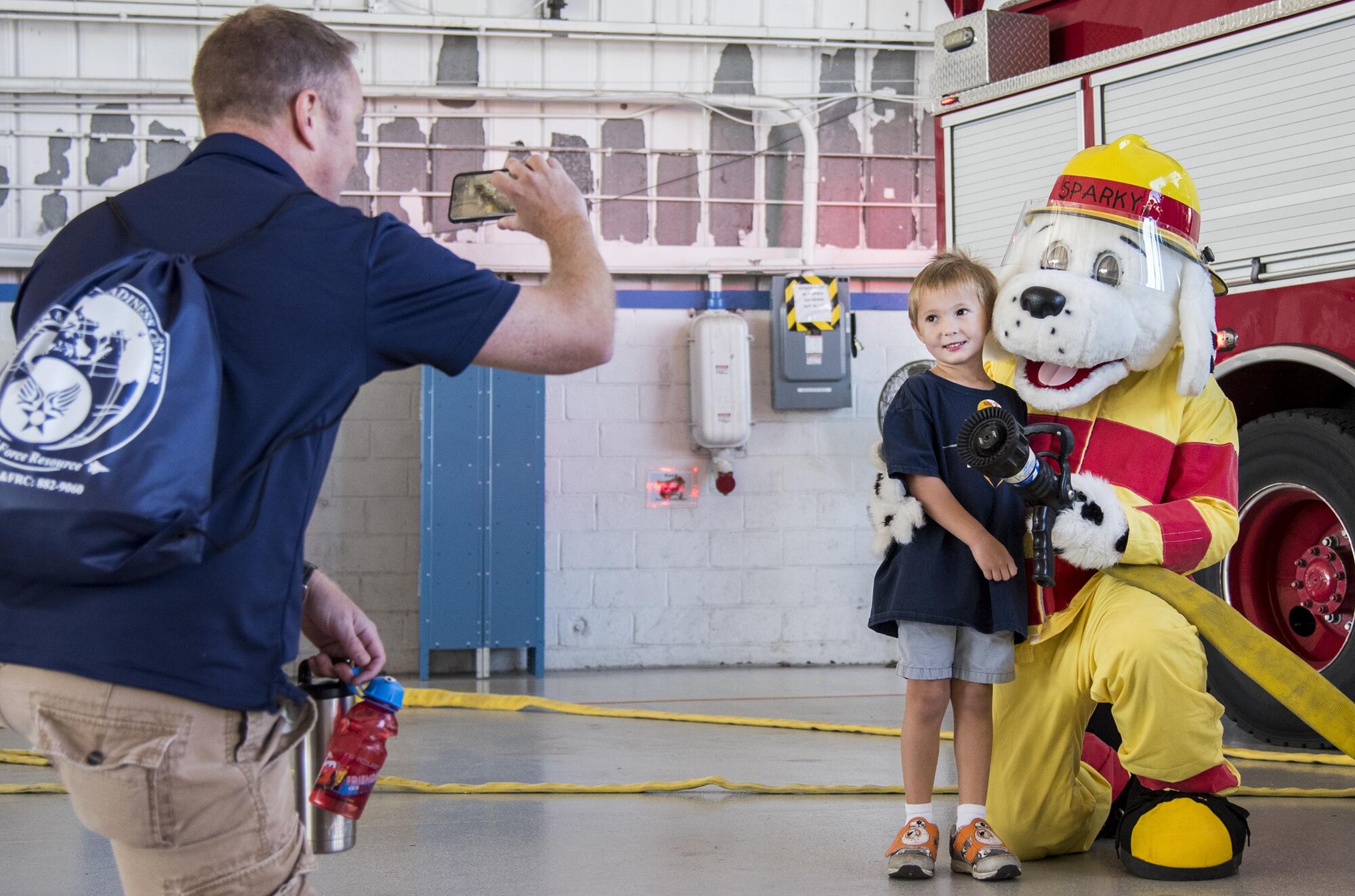 A proud father snaps a photo of his son with Sparky the Fire Dog during the Operation Hero event Oct. 22 at Eglin Air Force Base, Fla.  More than 100 kids participated in the mock deployment experience created to give military children a glimpse of what their loved ones go through when they leave home. The kids went through a deployment line to get their dog tags and “immunizations” before they were briefed by the commander and shipped off to a deployed location. There, they participated in various activities and demonstrations by local base agencies. (U.S. Air Force photo/Samuel King Jr.)