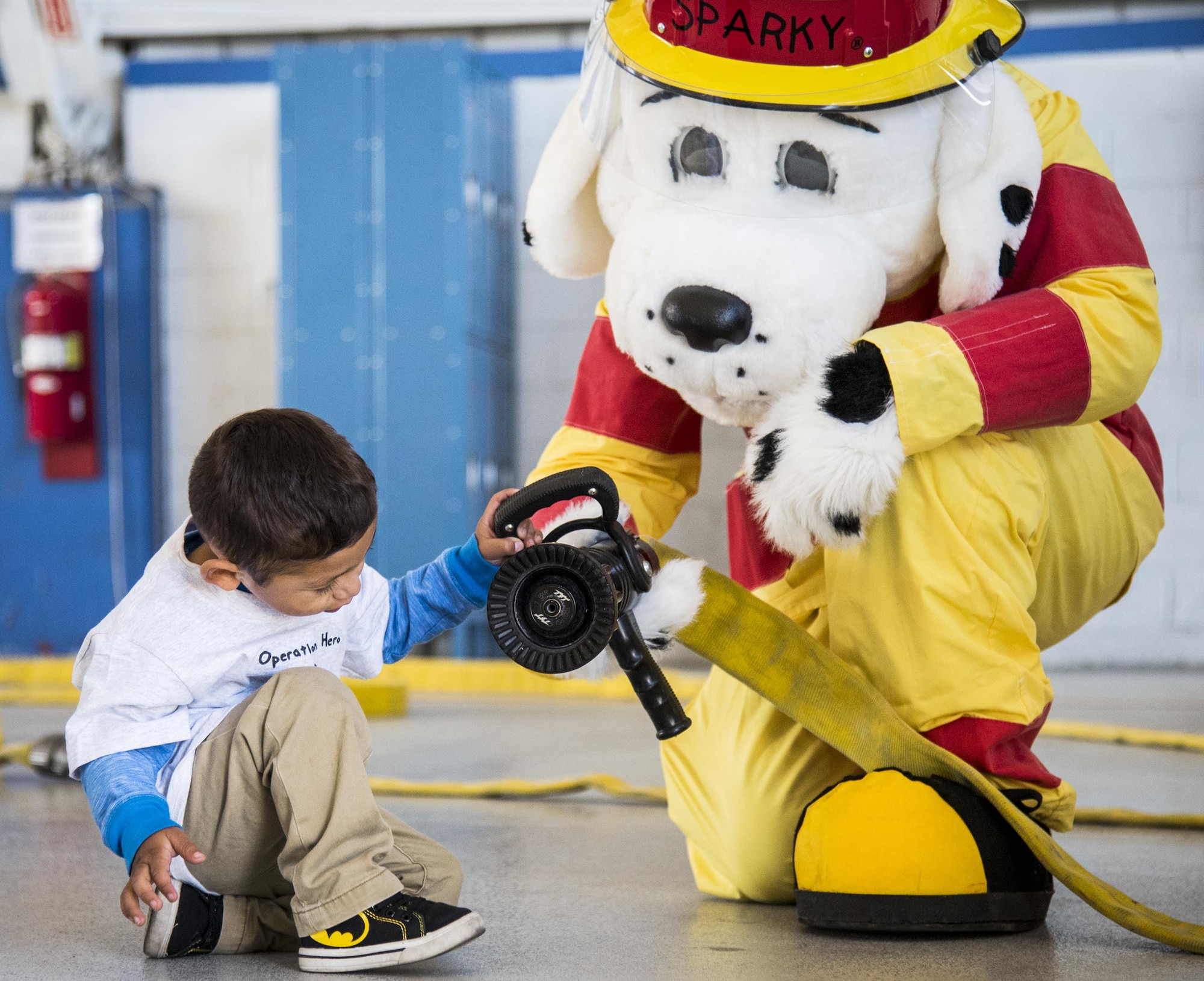 Sparky the Fire Dog explains how to use a fire hose to a new recruit during the Operation Hero event Oct. 22 at Eglin Air Force Base, Fla.  More than 100 kids participated in the mock deployment experience created to give military children a glimpse of what their loved ones go through when they leave home. The kids went through a deployment line to get their dog tags and “immunizations” before they were briefed by the commander and shipped off to a deployed location. There, they participated in various activities and demonstrations by local base agencies. (U.S. Air Force photo/Samuel King Jr.)