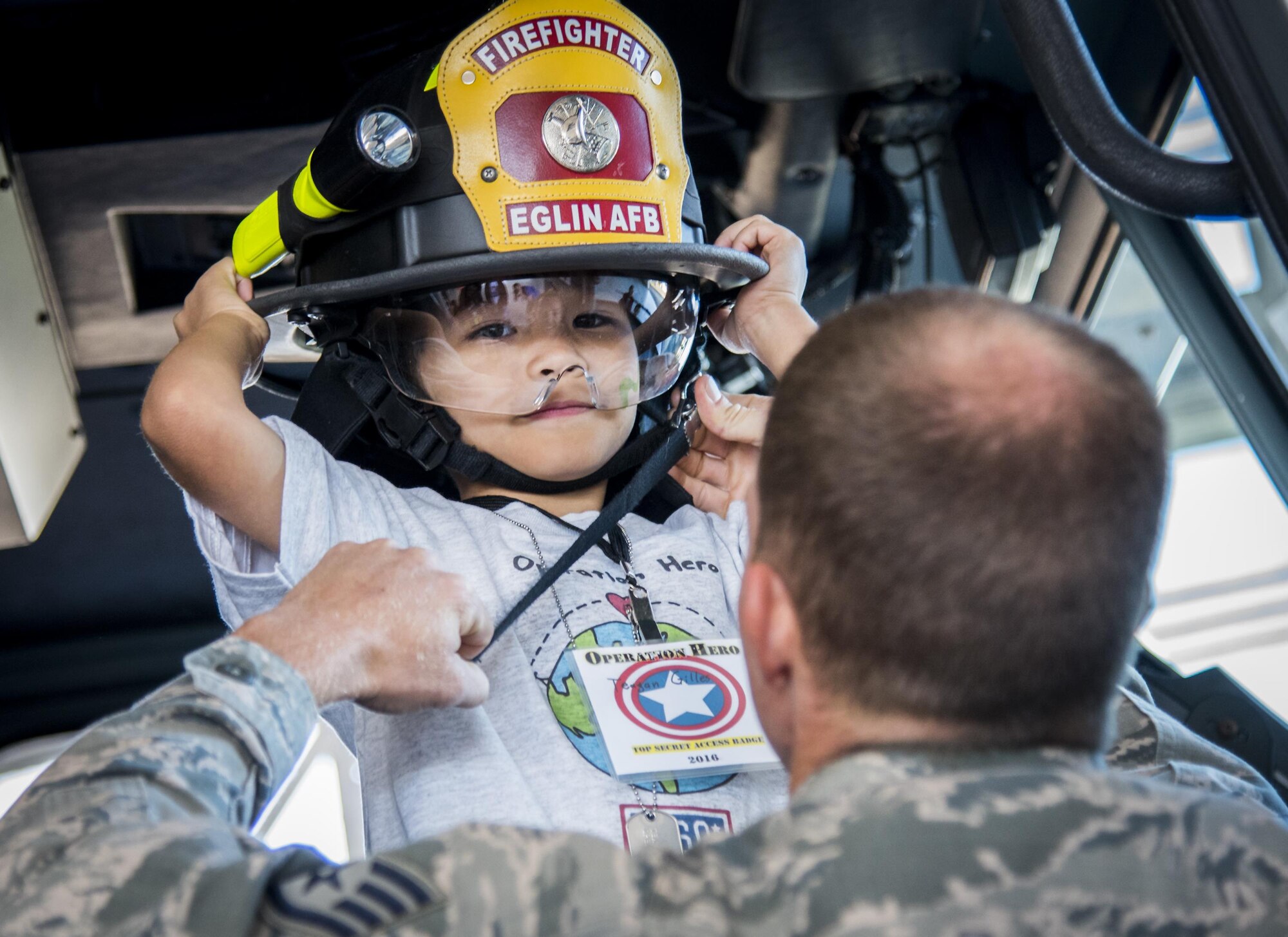 A staff sergeant helps a new recruit with his fire hat during the Operation Hero event Oct. 22 at Eglin Air Force Base, Fla.  More than 100 kids participated in the mock deployment experience created to give military children a glimpse of what their loved ones go through when they leave home. The kids went through a deployment line to get their dog tags and “immunizations” before they were briefed by the commander and shipped off to a deployed location. There, they participated in various activities and demonstrations by local base agencies. (U.S. Air Force photo/Samuel King Jr.)