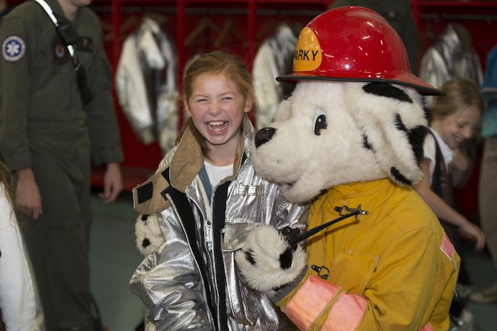Sparky, the fire dog for Marine Corps Air Station Iwakuni, poses for a picture with a Brownie from Iwakuni Brownies Troop 92 after trying on firefighting gear during a fire prevention and safety seminar on MCAS Iwakuni, Japan, Oct. 22, 2016. The Marines used methods the girls wouldn’t forget in their teaching such as interacting with Sparky, trying on the gear used for fighting fire and operating the fire hose. (U.S. Marine Corps photo by Lance Cpl. Joseph Abrego)