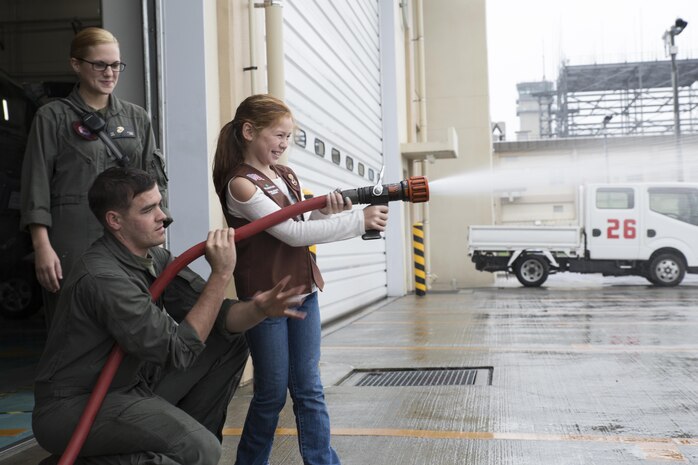 U.S. Marine Corps Lance Cpl. Allison Jenkins, firefighter specialist with Aircraft Rescue and Firefighting, watches U.S. Marine Corps Lance Cpl. Jacob Johnson, firefighter specialist with ARFF, while he ensures the safety of a Girl Scout from Iwakuni Brownies Troop 92 while operating a fire hose during a fire prevention and safety seminar at Marine Corps Air Station Iwakuni, Japan, Oct. 22, 2016. The Marines used methods the girls wouldn’t forget in their teaching such as interacting with Sparky, the fire dog for MCAS Iwakuni; trying on the gear used for fighting fire and operating the fire hose. (U.S. Marine Corps photo by Lance Cpl. Joseph Abrego)