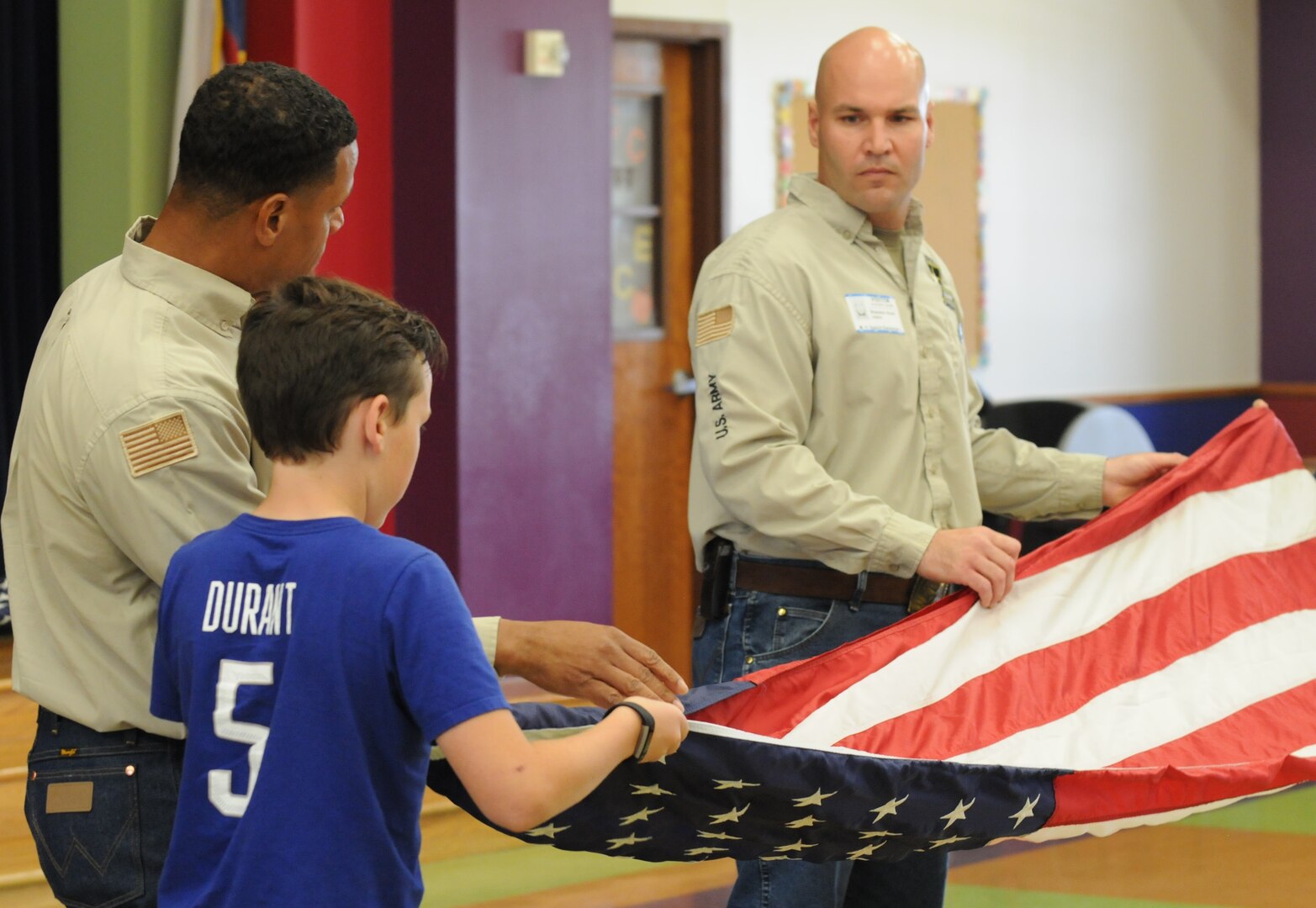 A fifth grader at Specht Elementary School in San Antonio is coached by Staff Sgt. Darren O. Thomas (left) and  Staff Sgt. Brandon Hood (right) from the Fort Sam Houston Honors Platoon Oct. 18 on how to properly fold the U.S. flag, as well as how to render proper honors when raising and lowering the flag. The students are volunteers with the task of putting up the flag in the mornings and taking it down at the end of each school day.