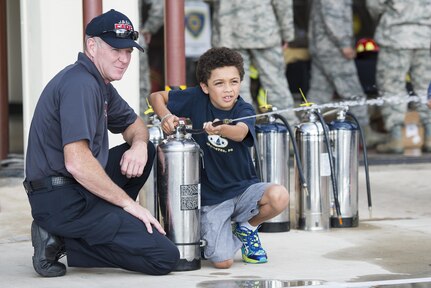 James Smith (left), Joint Base San Antonio-Randolph Fire Emergency Services fire inspector, assists Jaden Thiede put out a kitchen fire at the JBSA Fire Prevention Week open house at JBSA-Randolph Oct. 15, 2016. The National Fire Protection Association reported the leading cause of home structure fires are caused by cooking equipment. 