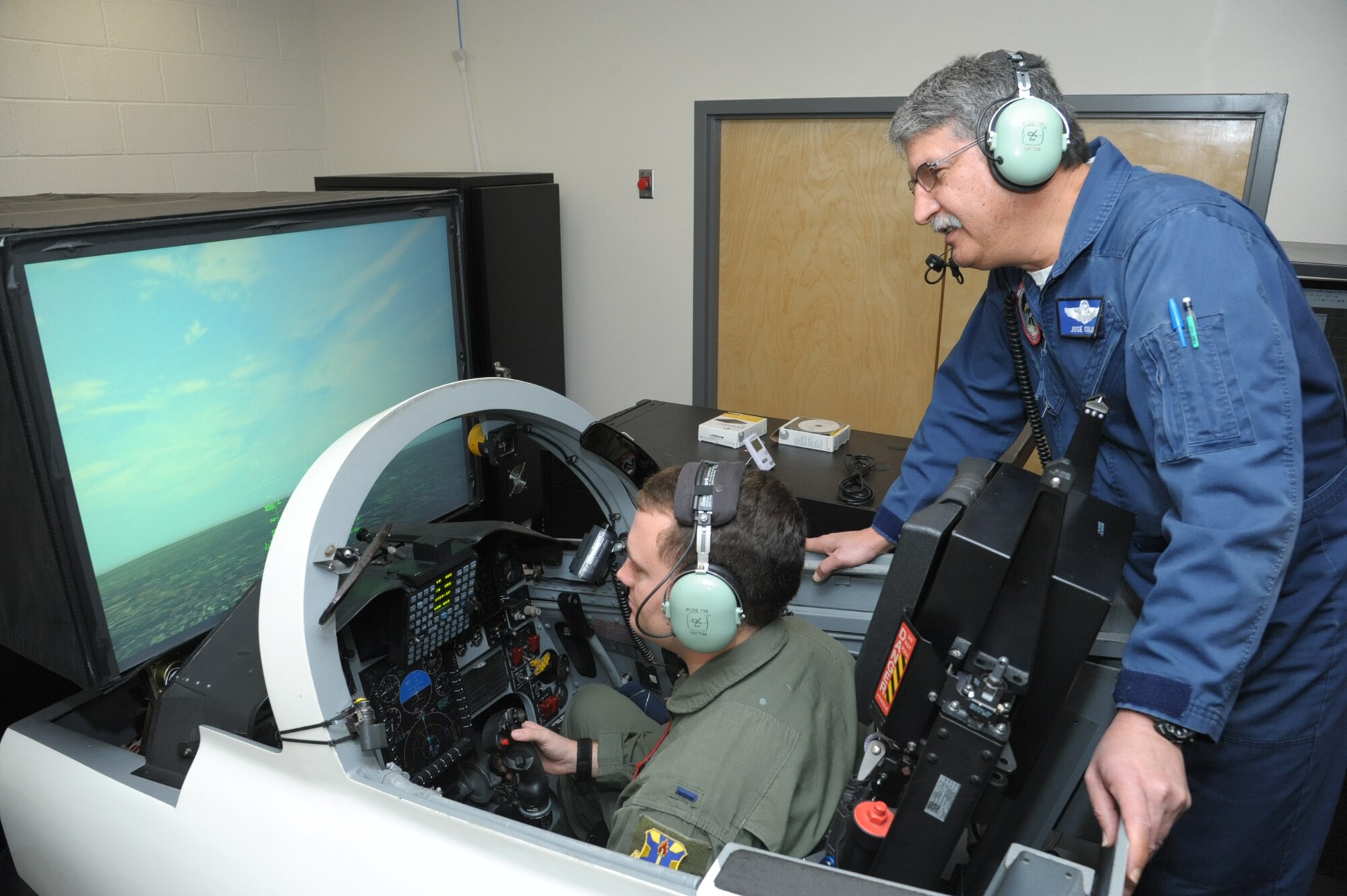 First Lt. Austin Hornsby,435th Flying Training Squadron student pilot trains on a simulator, while Jose Colon, instructor looks on, at Joint Base San Antonio-Randolph, Oct. 20, 2016. 	The simulator accomplishes less complex missions, such as instrument and emergency procedures training, due to the limited visual representation compared with the simulators known as the operational flight trainer and the weapon systems trainer.