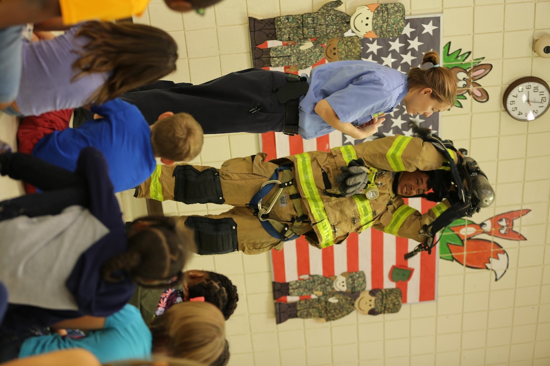 Brandee Ridgway (left) explains how fire safety equipment works as Raymond Bane dons his firefighting gear at W.J. Gurganus Elementary School in Havelock, N.C., Oct. 20, 2016. The Cherry Point Fire and Emergency Services Department visited the school to demonstrate what to do in fire emergencies and how to prevent them. The students also learned about the equipment firefighters use every day to complete their mission. Ridgway is a fire inspector, and Bane is a firefighter with the Cherry Point Fire and Emergency Services Department. (U.S. Marine Corps photo by Lance Cpl. Mackenzie Gibson/Released)