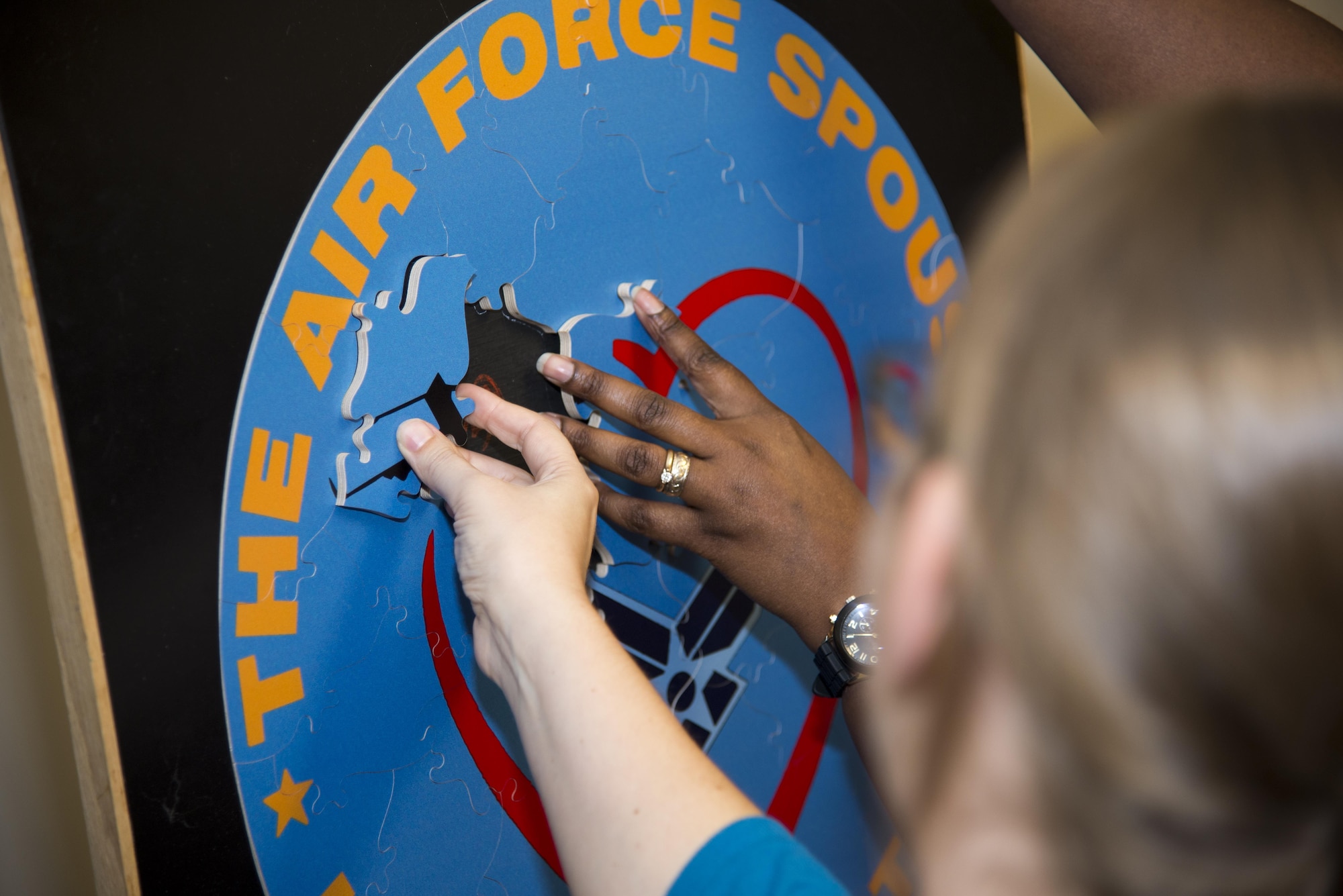 Team Dover spouses assemble a puzzle during Heartlink Oct. 19, 2016, at Chapel 1 on Dover Air Force Base, Del. Once complete, the puzzle forms the Heartlink spouse orientation program coin and symbolizes how the different pieces of Team Dover fit together; military members and their families. (U.S. Air Force photo by Staff Sgt. Jared Duhon) 